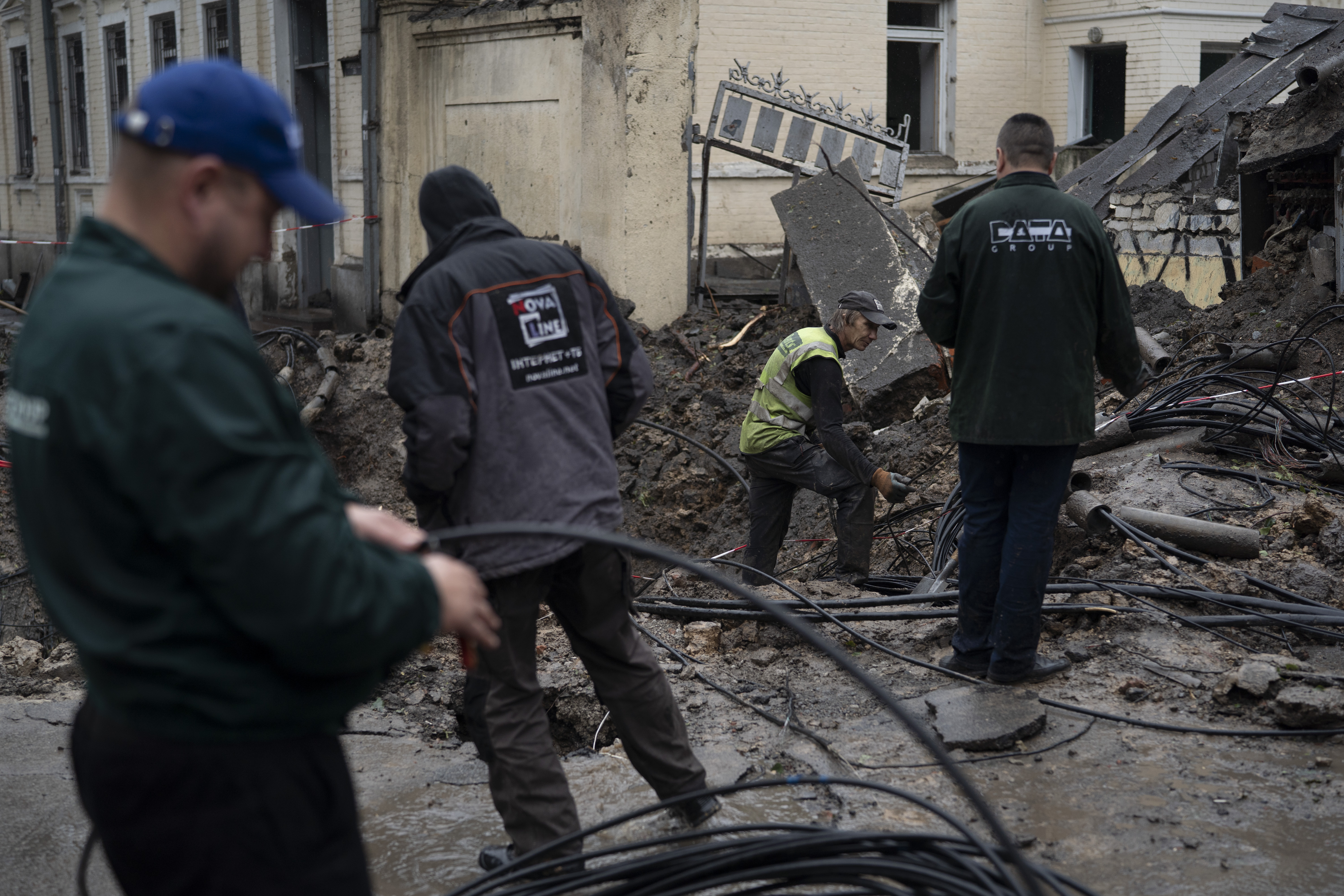 Men work next to a crater created by an explosion to fix the internet cables after a Russian attack in downtown, Kharkiv, Ukraine, Friday.