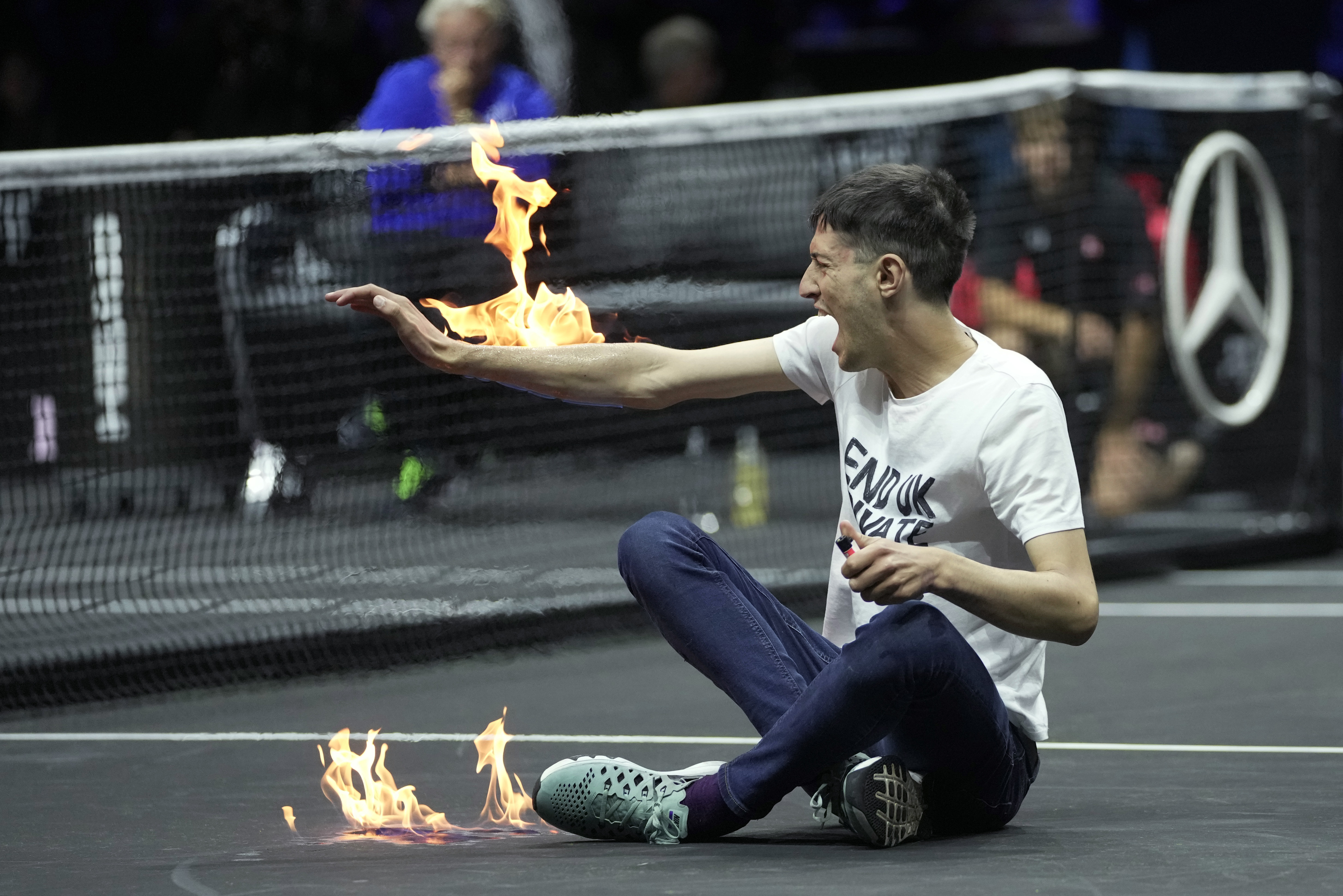 A man sets fire on his hand during protest at a match Team World's Diego Schwartzman against Team Europe's Stefanos Tsitsipas on day one of the Laver Cup tennis tournament at the O2 in London, Friday, Sept. 23, 2022. 