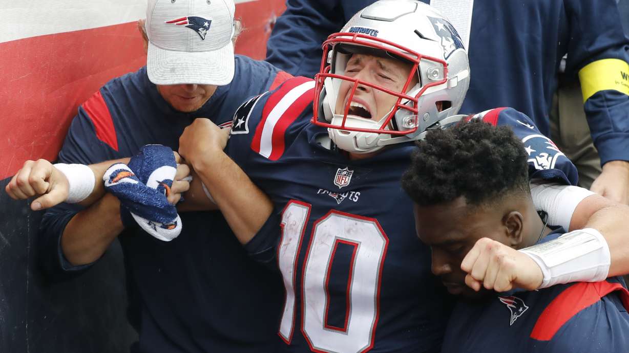New England Patriots quarterback Mac Jones (10) is helped off the field after suffering a leg injury with less than two minutes to play in the second half of an NFL football game against the Baltimore Ravens, Sunday, Sept. 25, 2022, in Foxborough, Mass.