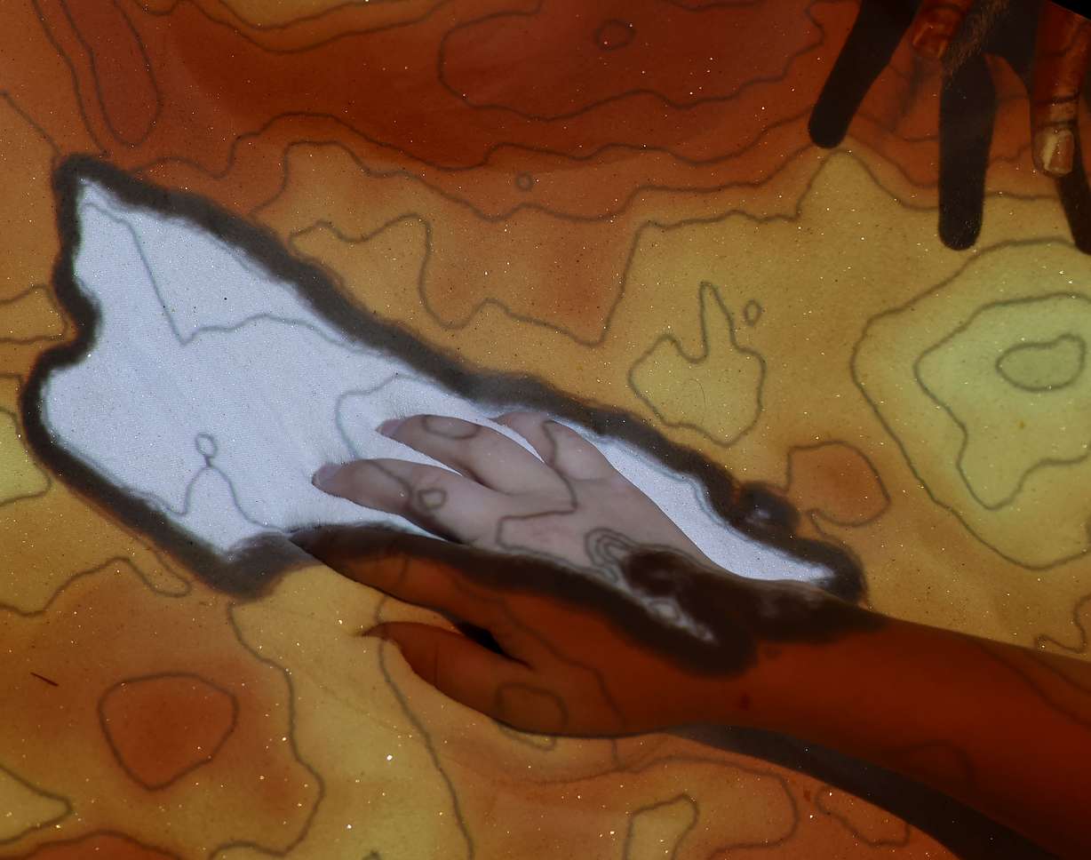 Students sift their hands through a 3D interactive topography map at the Utah Council of Land Surveyors booth at the eighth annual STEM Fest at the Mountain America Expo Center in Sandy on Tuesday.