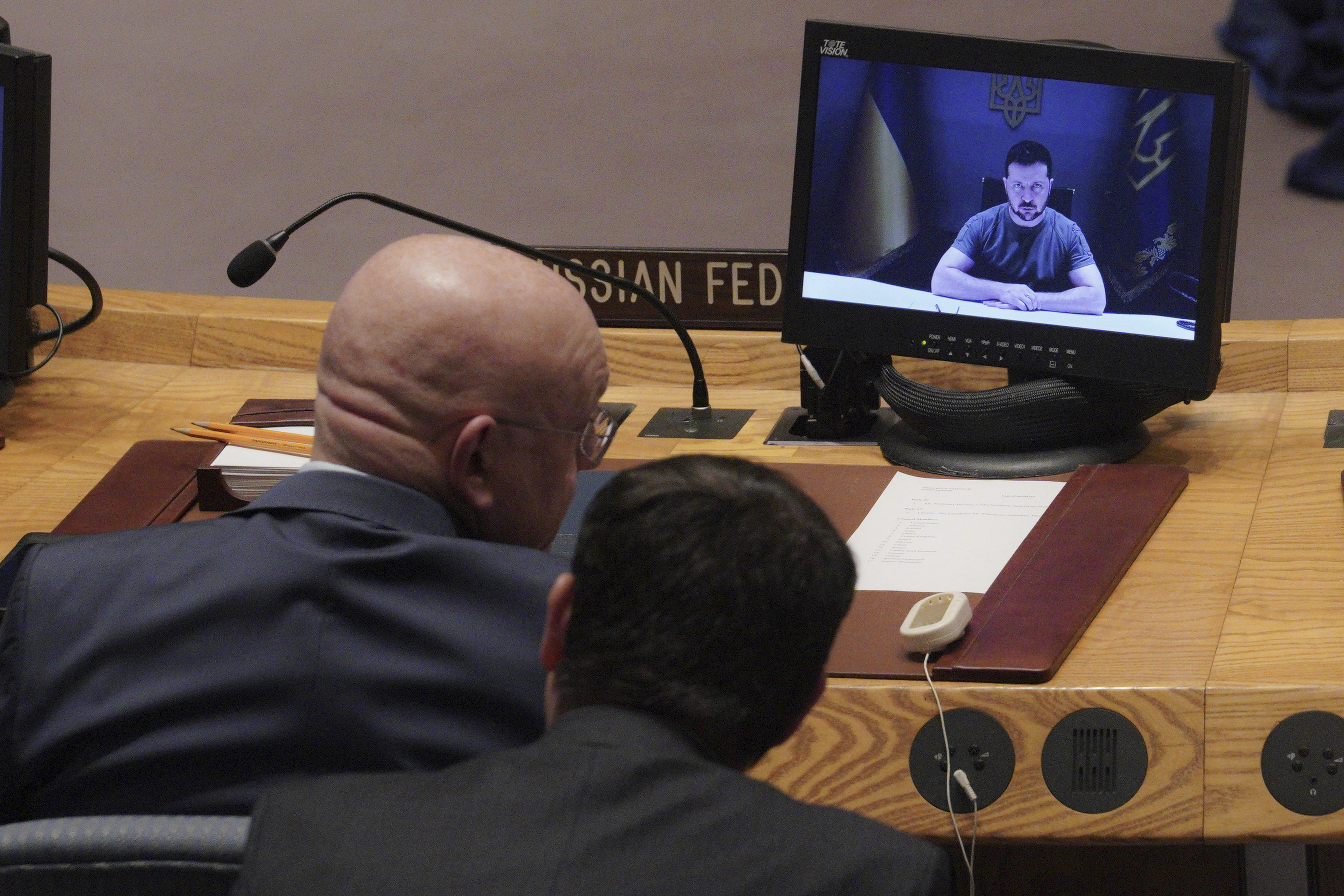 Russia's United Nations Ambassador Vasily Nebenzya, left, confers with an aide, while Ukraine President Volodymyr Zelenskyy addresses the United Nations Security Council by video, Tuesday, at U.N. headquarters. 