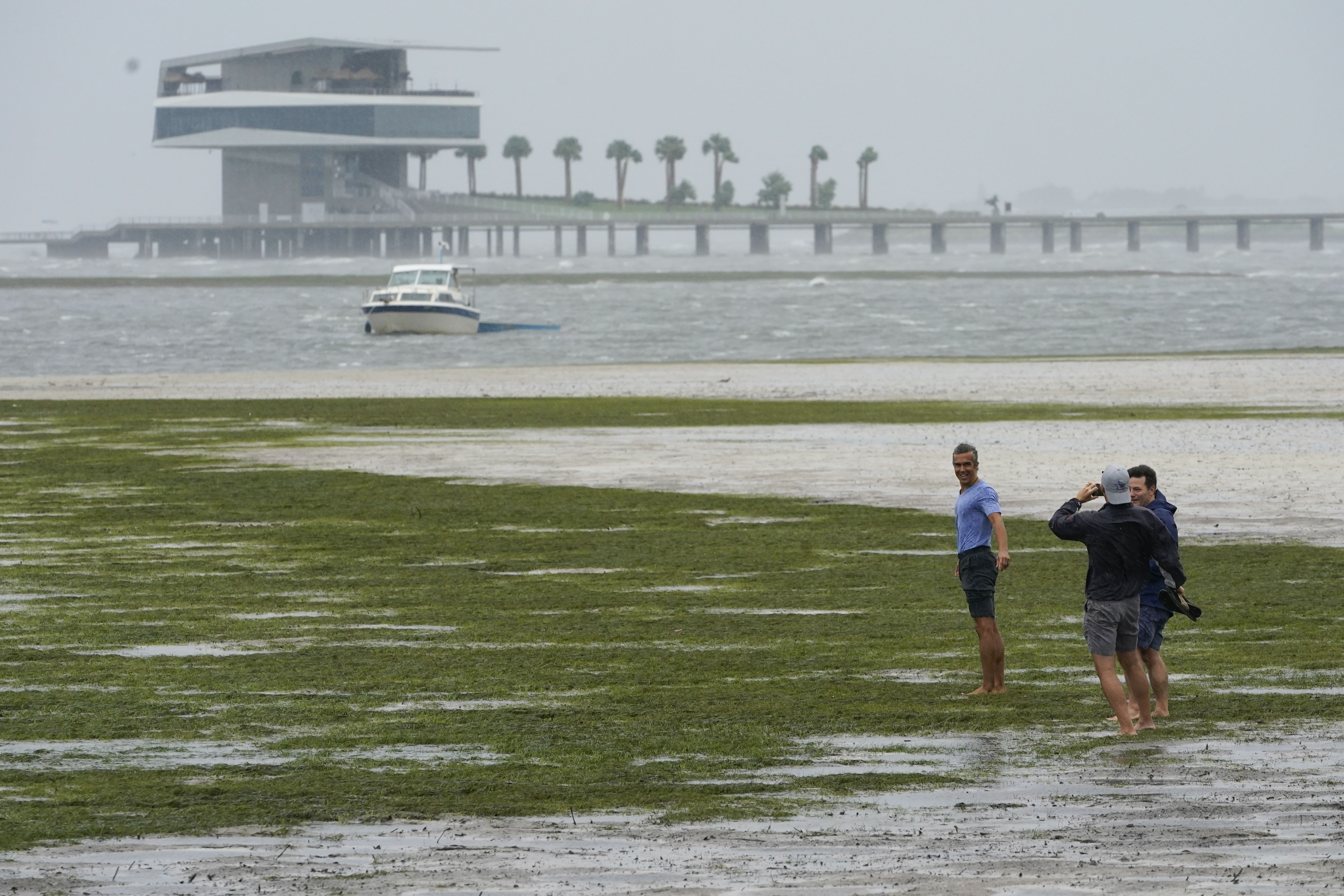 People walk where water is receding out of Tampa Bay due to a negative surge ahead of Hurricane Ian, Wednesday in Tampa, Fla.