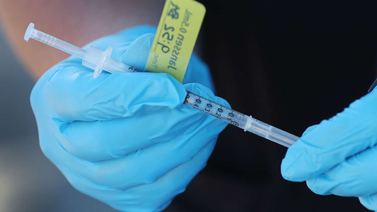 A syringe with a booster COVID-19 vaccine is held by a Nomi Health worker in West Valley City on July 14. Want an updated COVID-19 booster shot? Well, if you’ve recently had the virus, you’ll need to wait.