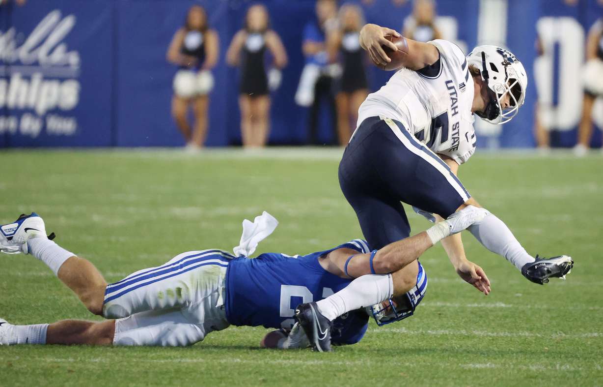Brigham Young Cougars defensive back Talan Alfrey (25) tackles Utah State Aggies quarterback Cooper Legas (5) in Provo on Thursday, Sept. 29, 2022.