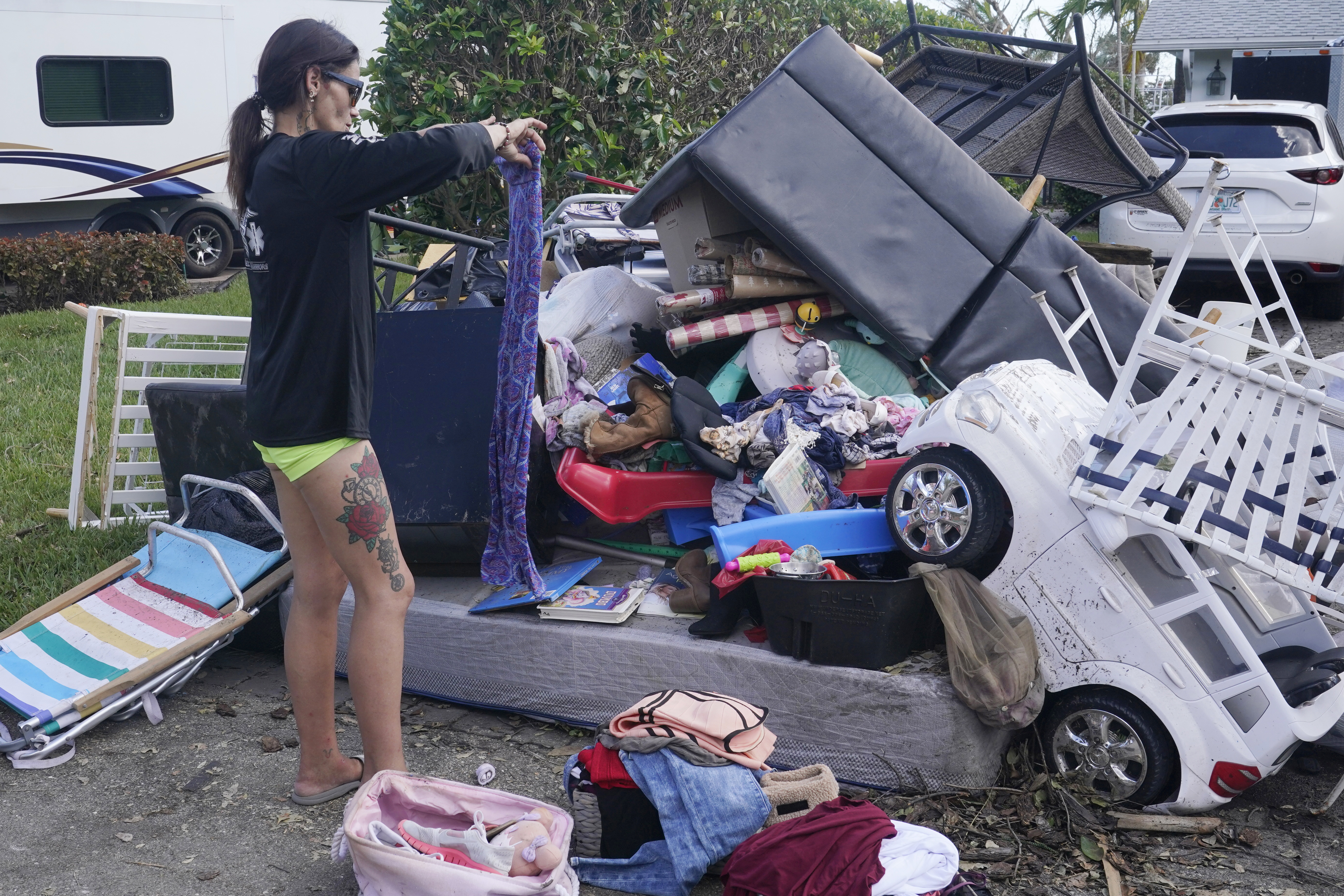 Alice Pujols goes through someone else's discarded items for clothes and shoes for her family Monday in Fort Myers, Fla. Pujols's home was completely destroyed after her home flooded due to rising waters caused by Hurricane Ian.