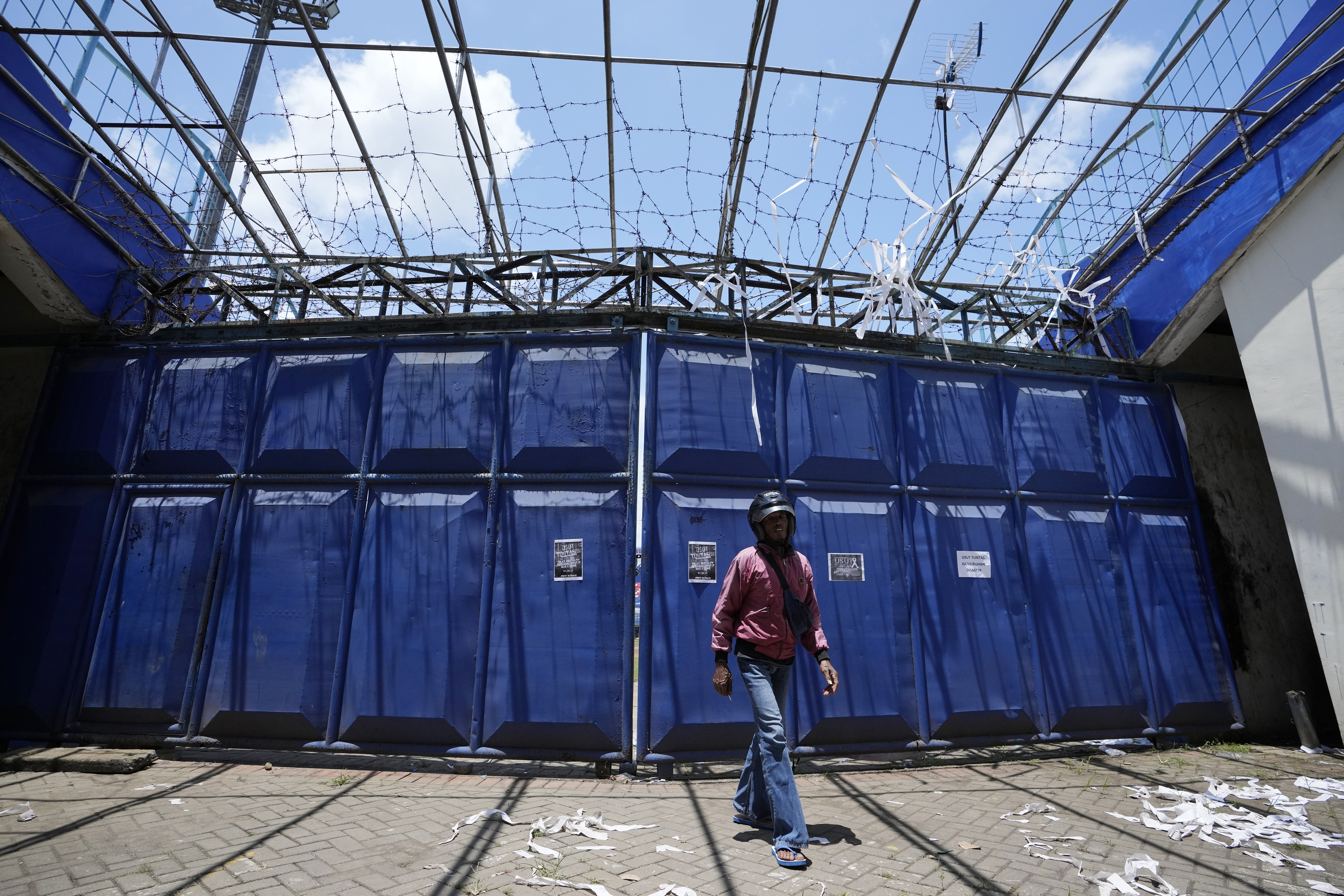 A man walks in front of gate at the Kanjuruhan Stadium in Malang, Indonesia, Tuesday, Oct. 4, 2022. A police chief and nine elite officers were removed from their posts Monday and 18 others were being investigated for responsibility in the firing of tear gas inside a soccer stadium that set off a stampede, killing over 100 people, officials said. 