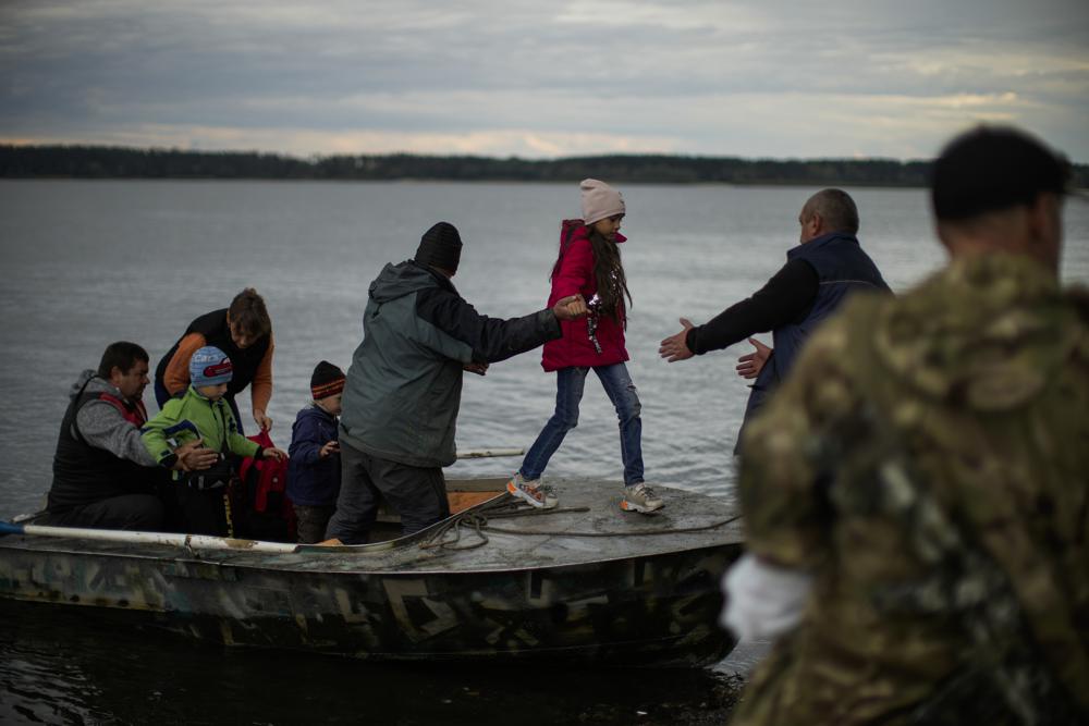 Yuri Shapovalov, center, helps people to disembark after crossing the Siverskyi-Donets river in Staryi-Saltiv, Ukraine, Wednesday. Shapovalov helps locals daily to cross the river with goods as the bridge was mostly destroyed during fighting.
