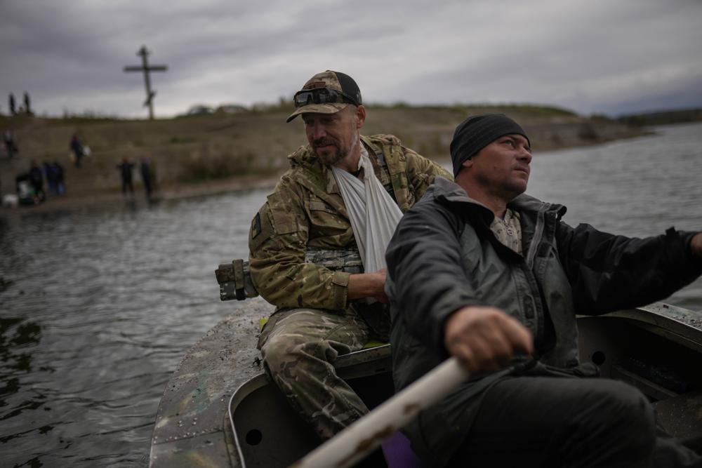 Yuri Shapovalov rows a boat carrying an injured Ukrainian serviceman and cross the Siverskyi-Donets river in Staryi-Saltiv, Ukraine, Wednesday. Shapovalov helps locals daily to cross the river with goods as the bridge was mostly destroyed during fighting.