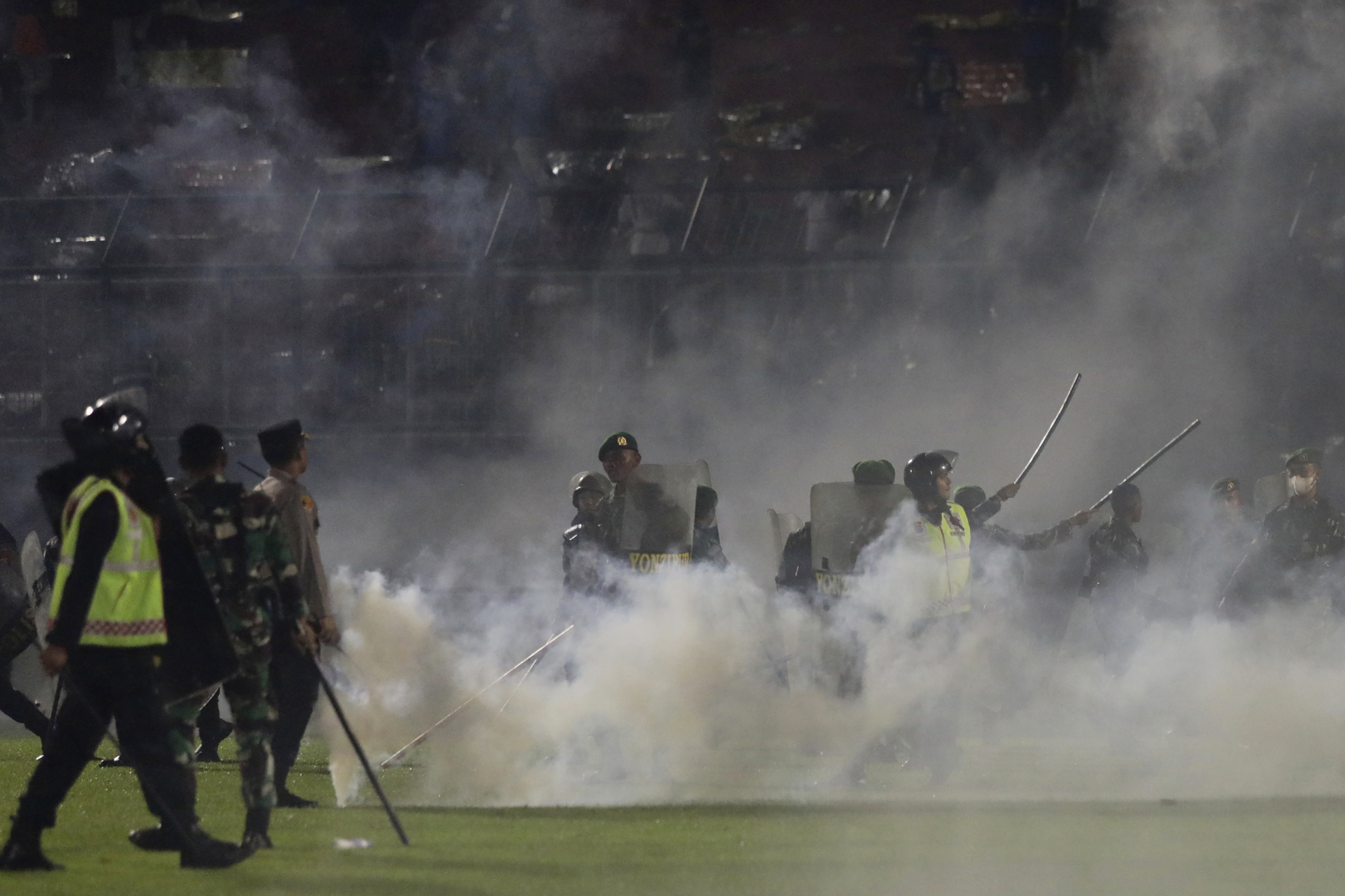 FILE - Police officers and soldiers stand amid tear gas smoke after clashes between fans during a soccer match at Kanjuruhan Stadium in Malang, East Java, Indonesia, Saturday, Oct. 1, 2022. 