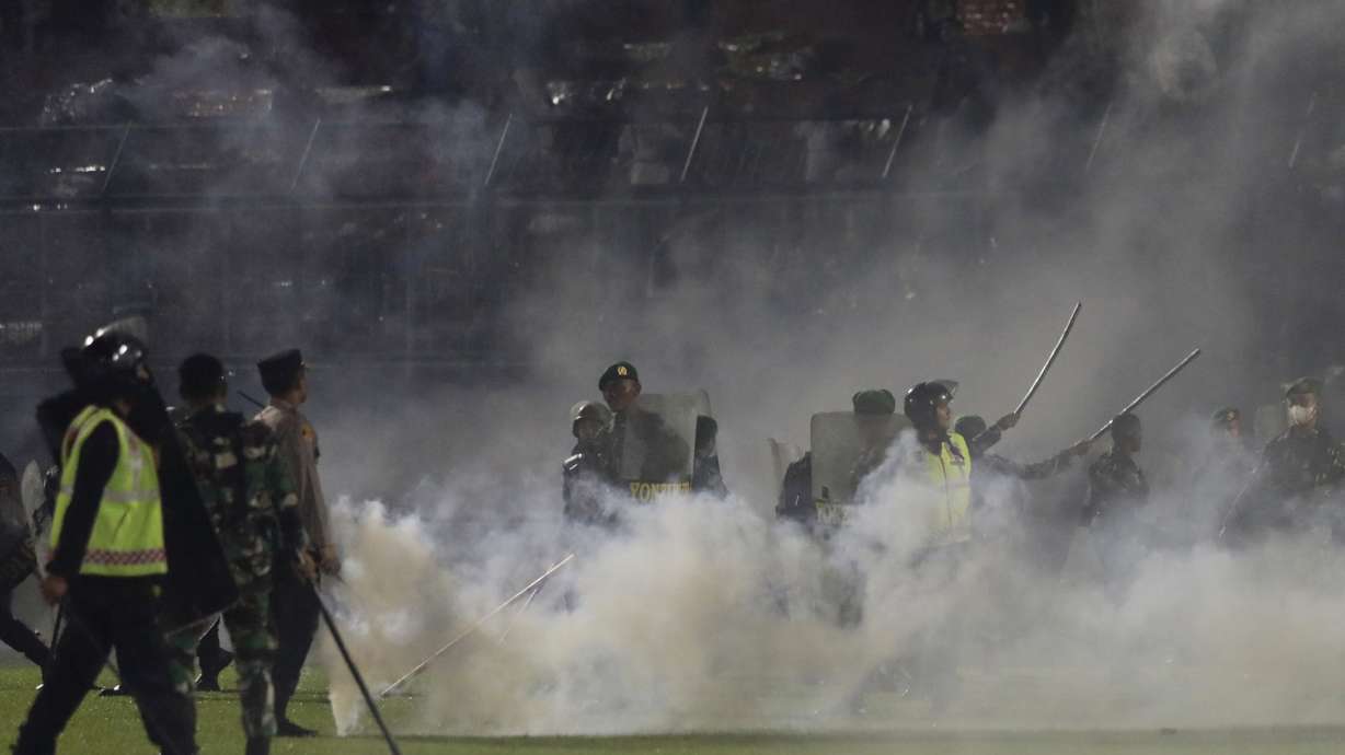FILE - Police officers and soldiers stand amid tear gas smoke after clashes between fans during a soccer match at Kanjuruhan Stadium in Malang, East Java, Indonesia, Saturday, Oct. 1, 2022.