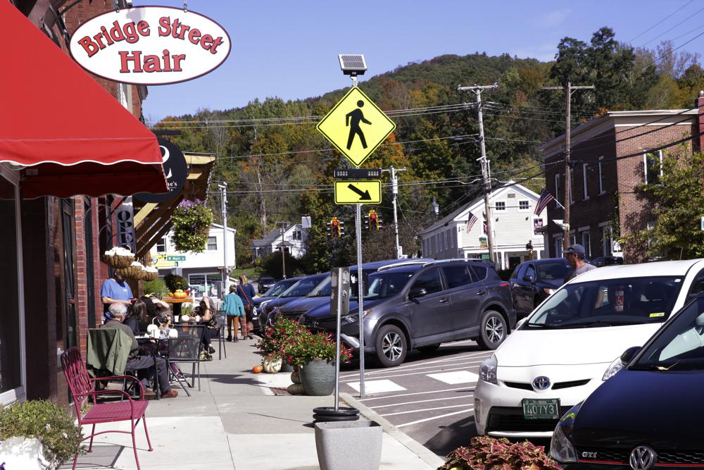 People walk past cafe table as cars park curbside, Wednesday in Richmond, Vt. A town employee in Richmond is under fire for lowering the fluoride level in the drinking water below the state's recommended level for more than three years. A town commission has voted to return the water to full fluoridation after outrage from some residents.