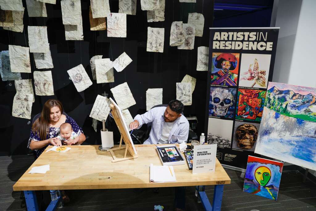 Walter Cifuentes García paints while his partner, Crystal Masaquaptewa, holds their 8-month-old son, Mateo Masaquaptewa-Cifuentes, at The Leonardo on Saturday.