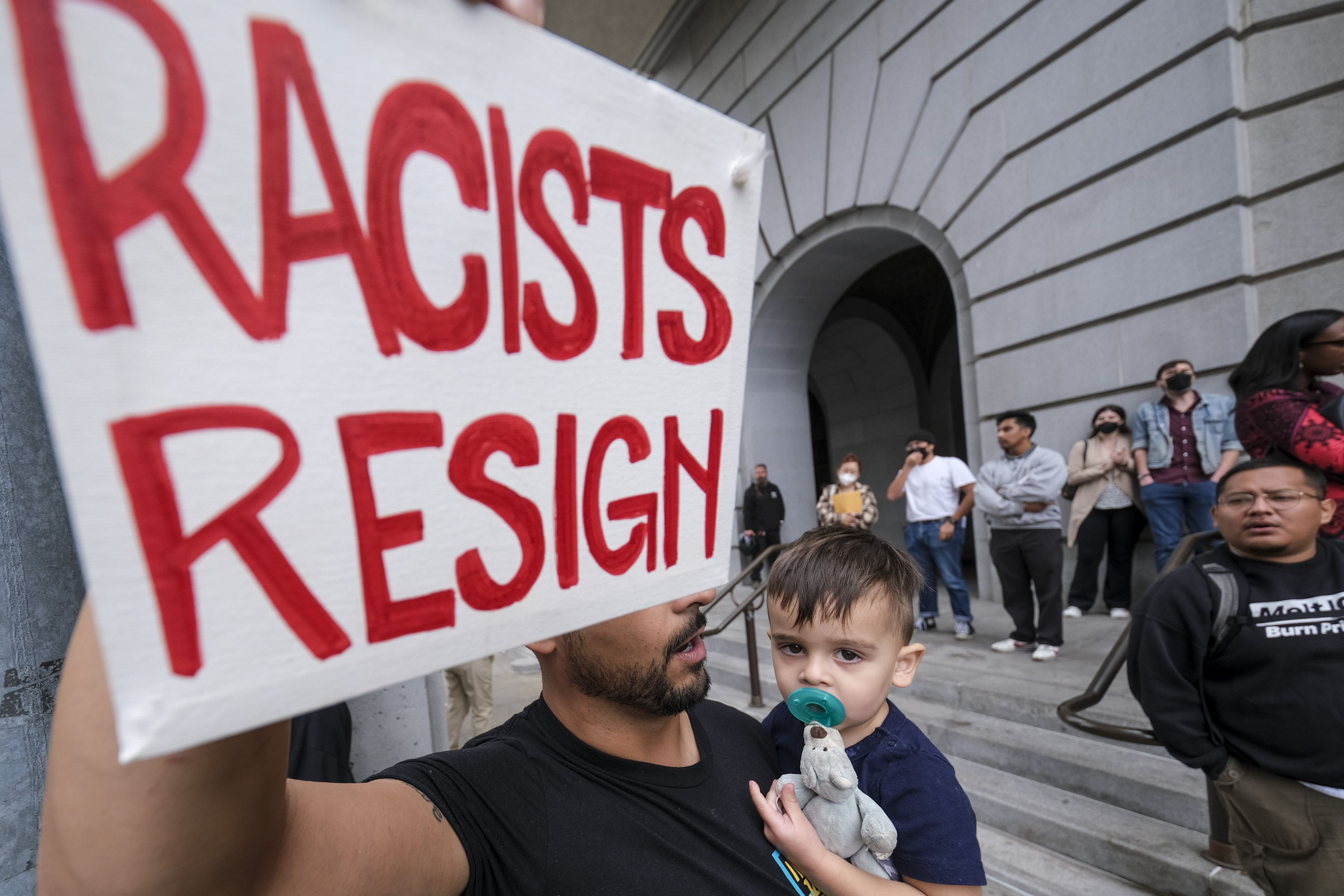 Shervin Aazami holding his son Barrett and a sign protest outside City Hall during the Los Angeles City Council meeting Tuesday in Los Angeles. Former Council President Nury Martinez has announced that she is resigning her council seat.