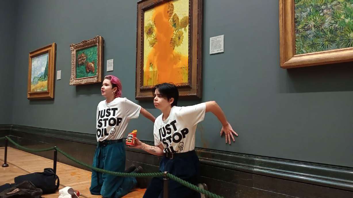 In this image released by the Just Stop Oil organization, two women are seen standing in front of Van Gogh's "Sunflowers" (1888) in a London gallery Friday. The anti-fossil fuel protesters were filmed throwing tomato soup on the artwork Friday and have since been charged with criminal damage offenses.