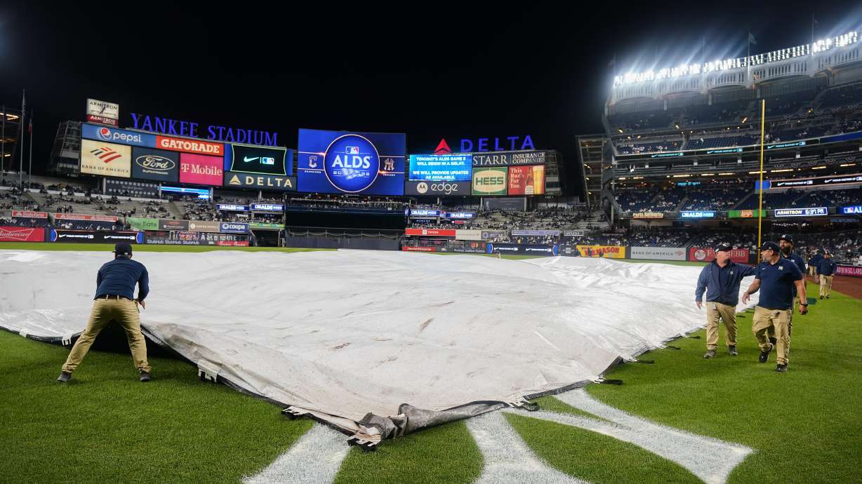 The Yankee Stadium grounds crew pulls the rain tarp over the field during a rain delay before Game 5 of an American League Division baseball series between the New York Yankees and the Cleveland Guardians, Monday, Oct. 17, 2022, in New York.