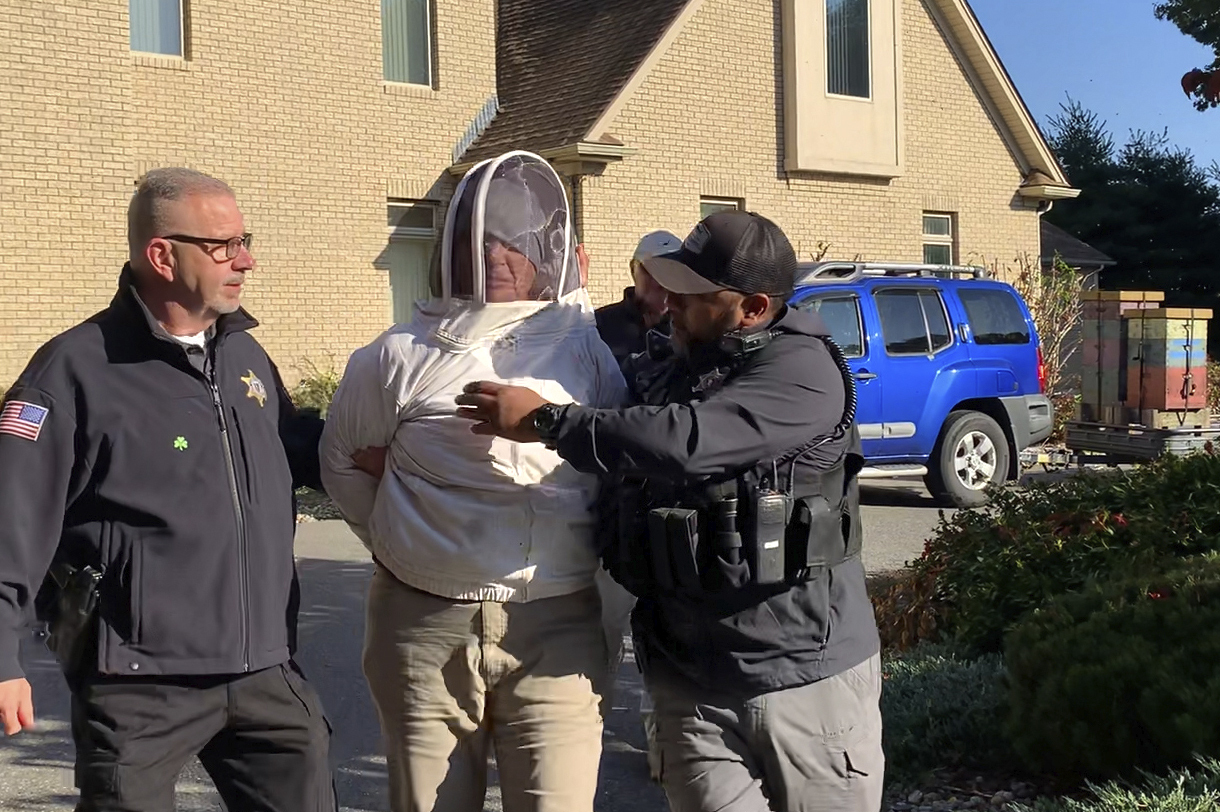 Rorie S. Woods, 55, of Hadley, Mass., center, wears a beekeeping suit while taken into custody by Hampden County Sheriff's Department officers, in Longmeadow, Mass., Wednesday. Woods is facing multiple assault and battery charges for allegedly unleashing a swarm of bees on a group of sheriff's deputies.