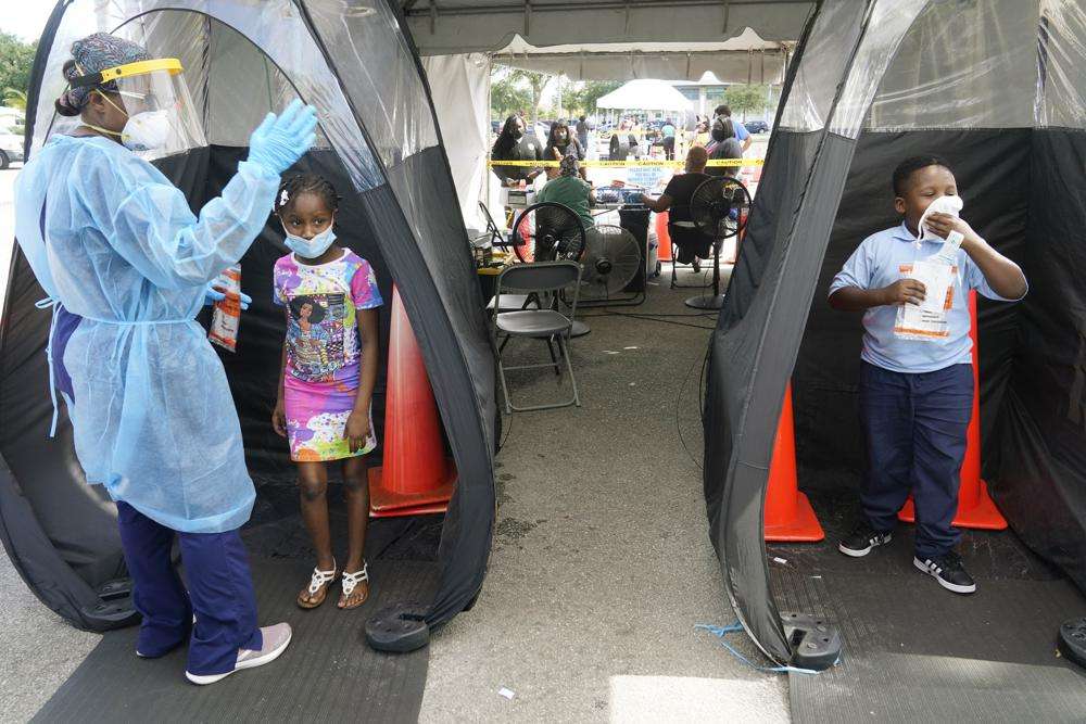 Wenderson Cerisene, 7, right, and his sister Dorah, 9, wait to be tested for COVID-19, Aug. 31, 2021, in North Miami, Fla. In interviews with The Associated Press, close to 50 school leaders, teachers, parents and health officials reflected on decisions to keep students in extended online learning, especially during the spring semester of 2021.