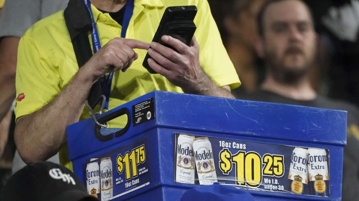 A beer vendor figures out the price for a baseball fan during a baseball game between the Cleveland Guardians and Chicago White Sox Tuesday, Sept. 20, 2022, in Chicago. Persistently high inflation and gas prices are looming over sports and the monetary pipeline that resumed when fans returned to games amid the pandemic.