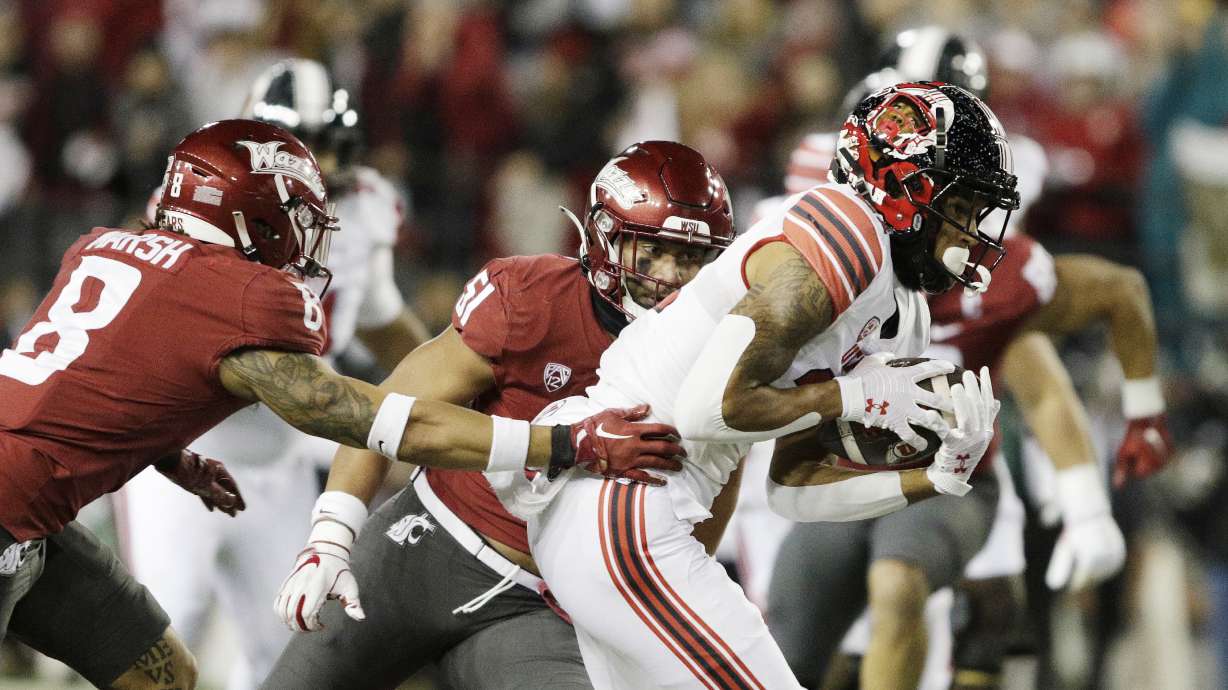 Utah wide receiver Solomon Enis, right, carries the ball while pressured by Washington State defensive back Armani Marsh, left, and linebacker Francisco Mauigoa during the first half of an NCAA college football game, Thursday, Oct. 27, 2022, in Pullman, Wash.