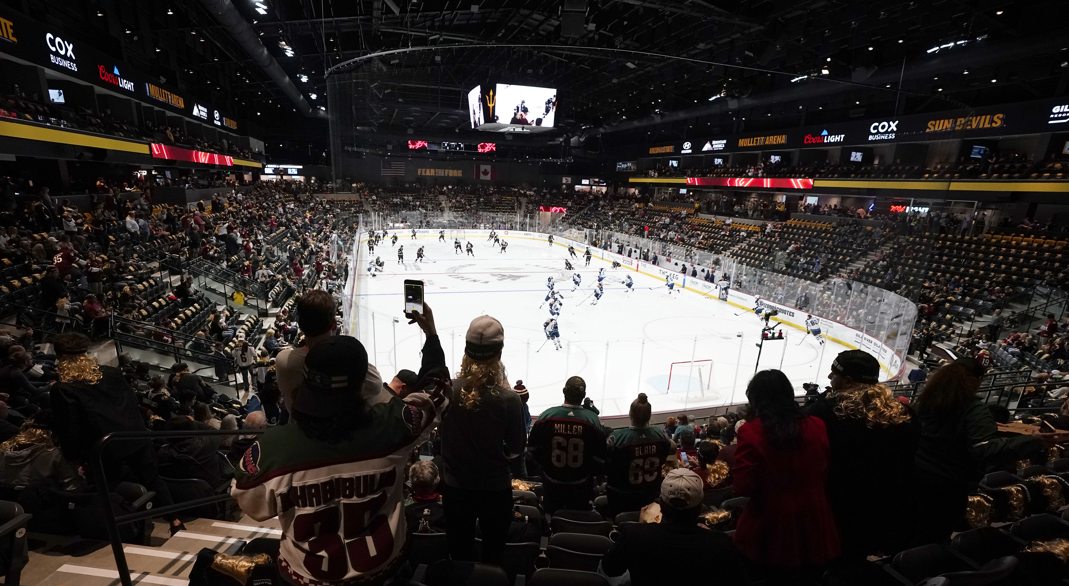 Fans watch players as they warm up prior to the Arizona Coyotes NHL home-opening hockey game against the Winnipeg Jets at the 5,000-seat Mullett Arena in Tempe, Ariz., Friday, Oct. 28, 2022. The Coyotes will share the arena with the Arizona State NCAA college hockey team.