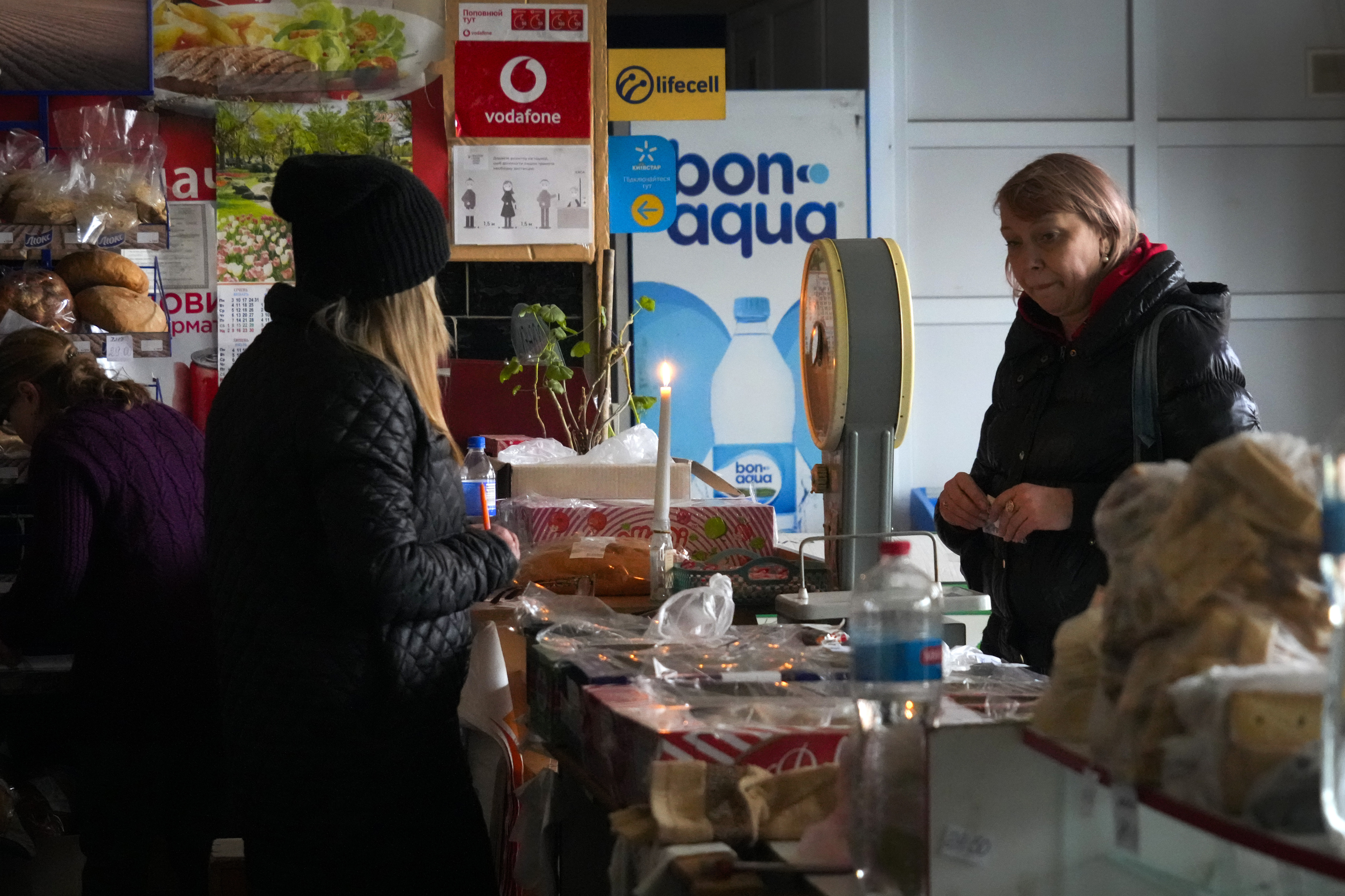A local resident buys food products over a shop counter, lit by a candle, on the outskirts of Bakhmut, the site of the heaviest battle against the Russian troops in the Donetsk region, Ukraine, Friday. 