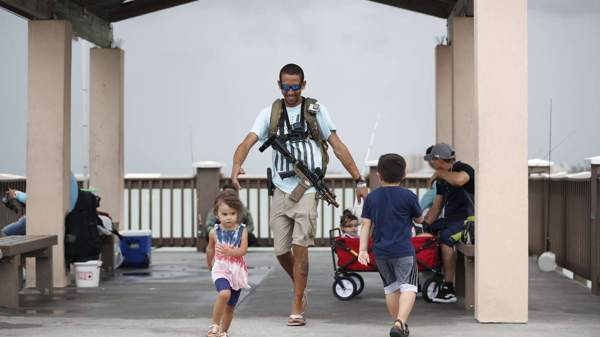 Michael Taylor, also known as "The Armed Fisherman," walks along Pier 60 in Clearwater Beach, Fla., with his 2-year-old daughter Ocean and his assault rifle and fishing gear, on July 3, 2021. Advocates say permitless carry makes people safer. Opponents say it makes it more dangerous for ordinary people, and for police officers.