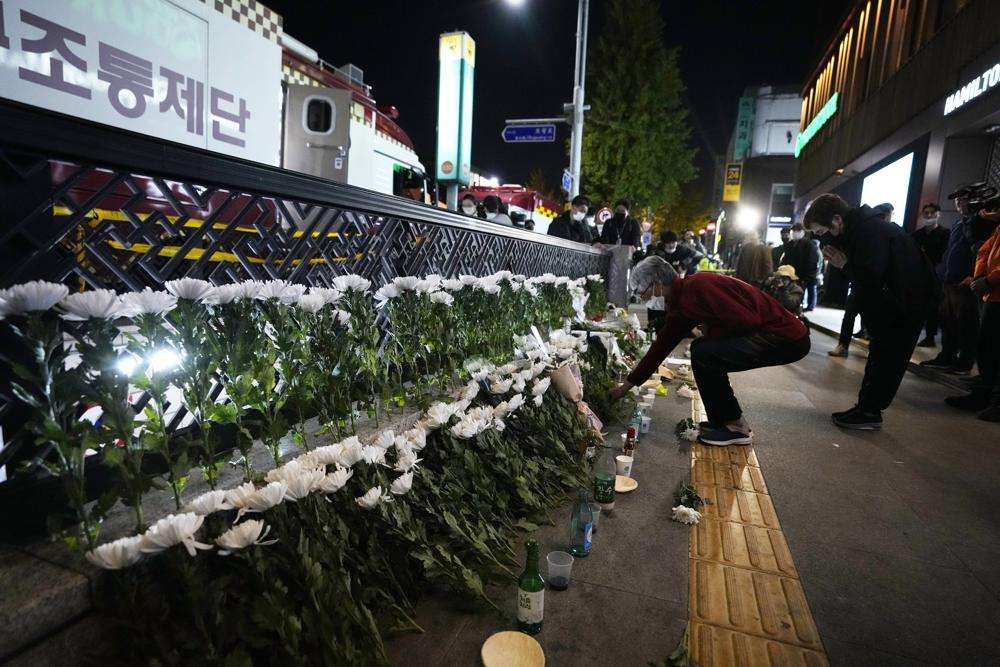 A woman places flowers to pay tribute to victims near the scene of a deadly accident in Seoul, South Korea, Sunday, following Saturday night's Halloween festivities. A mass of mostly young people among tens of thousands who gathered to celebrate Halloween in Seoul became trapped and crushed as the crowd surged into a narrow alley, killing dozens of people and injuring dozens of others in South Korea’s worst disaster in years.