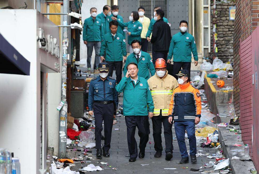 South Korean President Yoon Suk Yeol, center left, visits the scene where dozens of people died and were injured in Seoul, South Korea, Sunday, after a mass of mostly young people celebrating Halloween festivities became trapped and crushed as the crowd surged into a narrow alley.