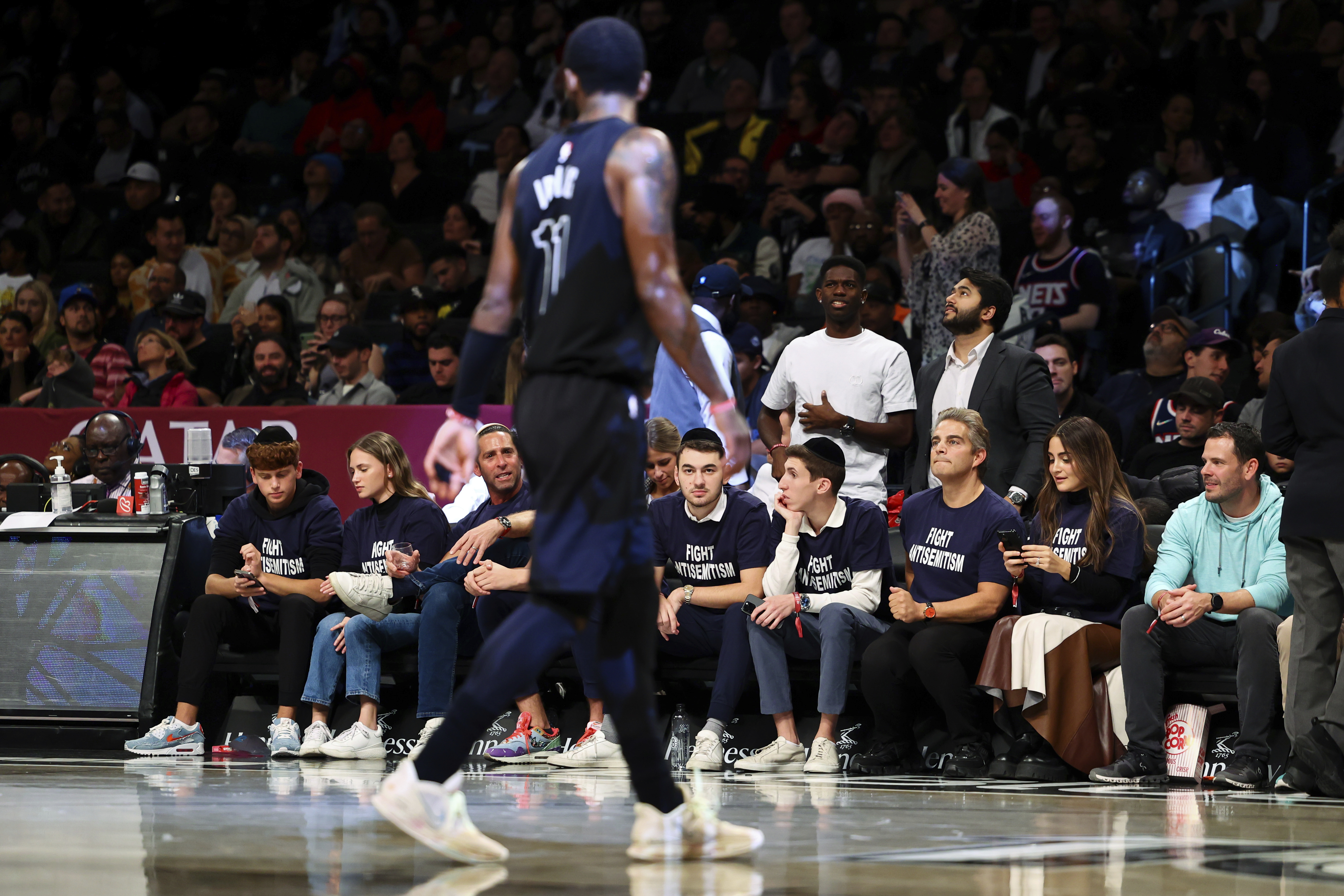 Fans with matching shirts look on as Brooklyn Nets guard Kyrie Irving (11) walks by during the first half of an NBA basketball game against the Indiana Pacers, Monday, Oct. 31, 2022, in New York. 