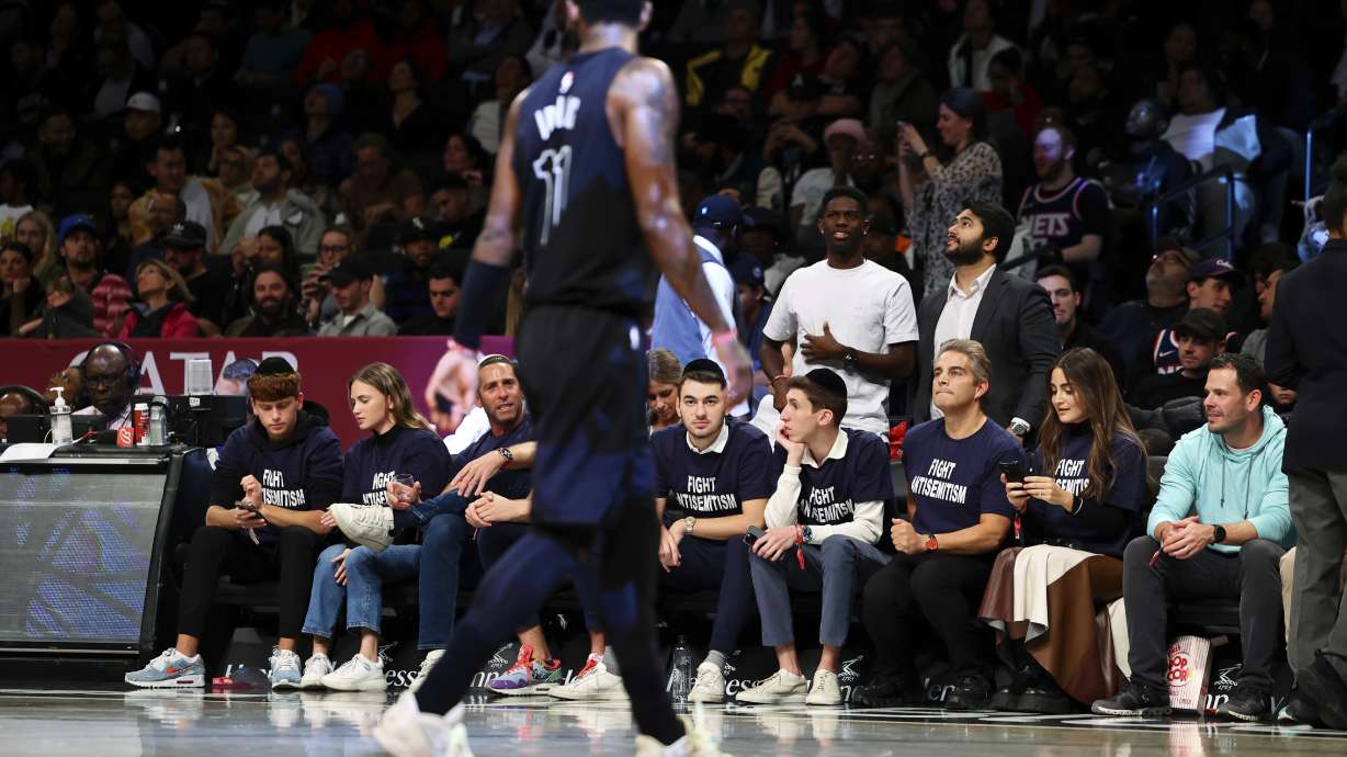 Fans with matching shirts look on as Brooklyn Nets guard Kyrie Irving (11) walks by during the first half of an NBA basketball game against the Indiana Pacers, Monday, Oct. 31, 2022, in New York.