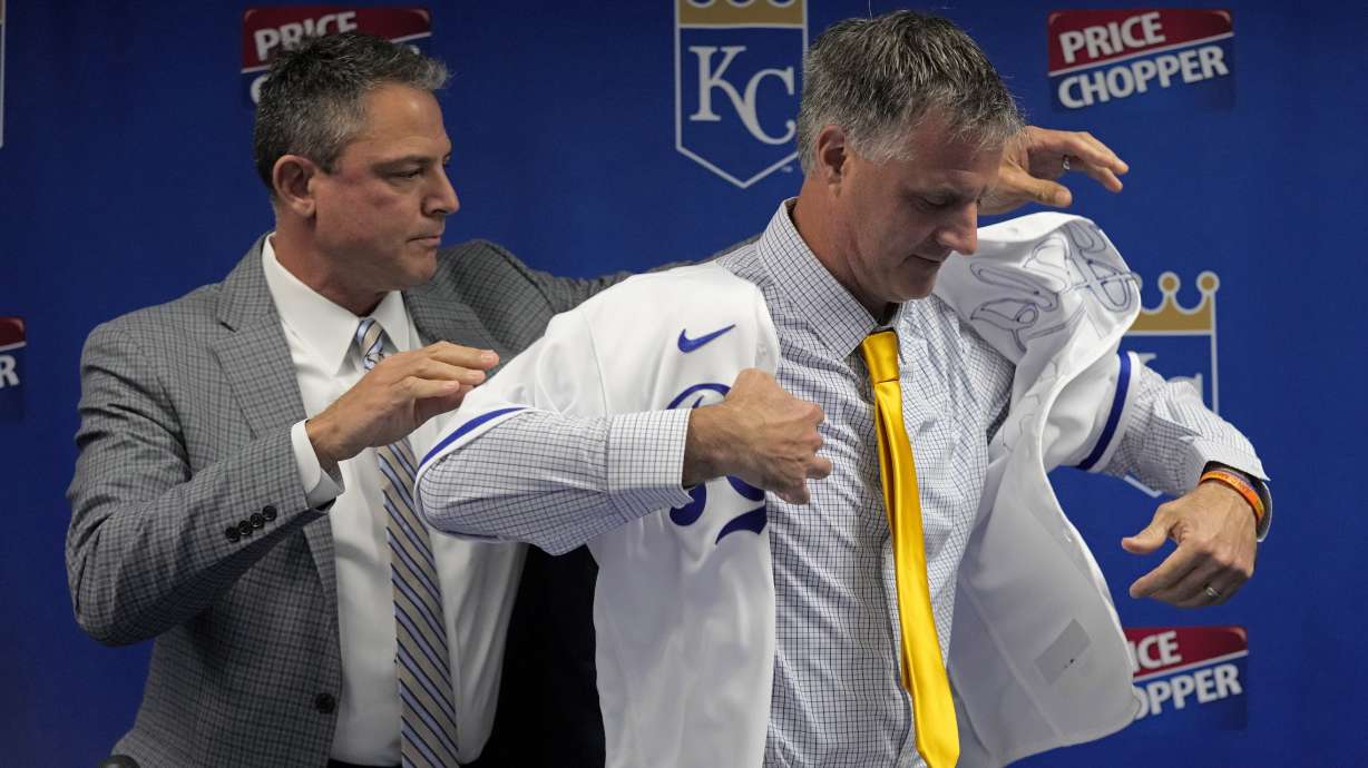 Matt Quatraro is helped by general manager J.J. Piccolo as he tries on a jersey during a news conference announcing him as the new manager of the Kansas City Royals Thursday, Nov. 3, 2022, in Kansas City, Mo.