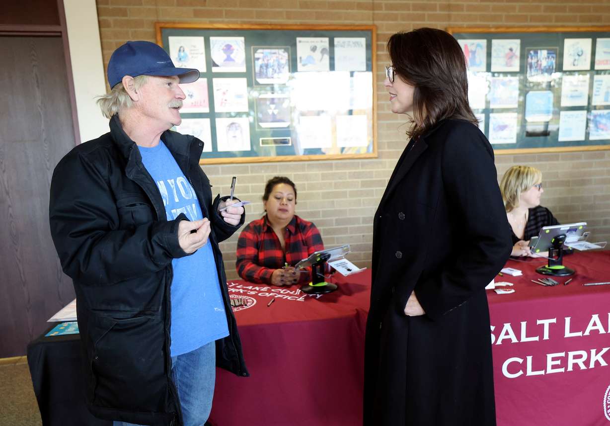 Mike Lyons, left, talks with Lt. Gov. Deidre Henderson while waiting to vote at the Salt Lake County Government Center in Salt Lake City on Thursday.
