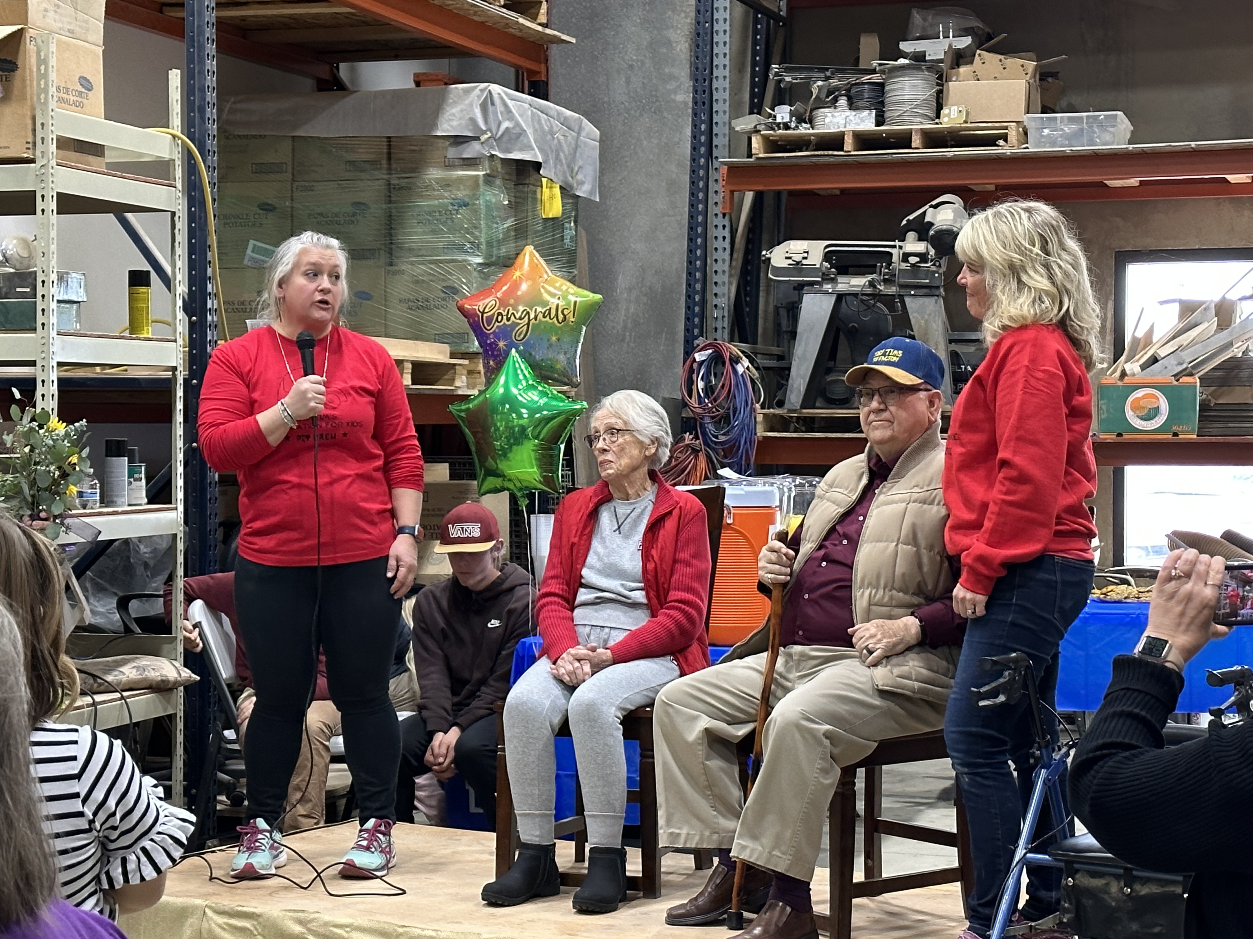 Cheryl and Alton Thacker, sitting, listen to their daughter Ashley Krause speak during a retirement party for them on Saturday. The Thackers are passing on ownership of Tiny Tim's Foundation for Kids to Krause and their granddaughter Emilee Johnson who will continue building wooden toys to give to kids in need.