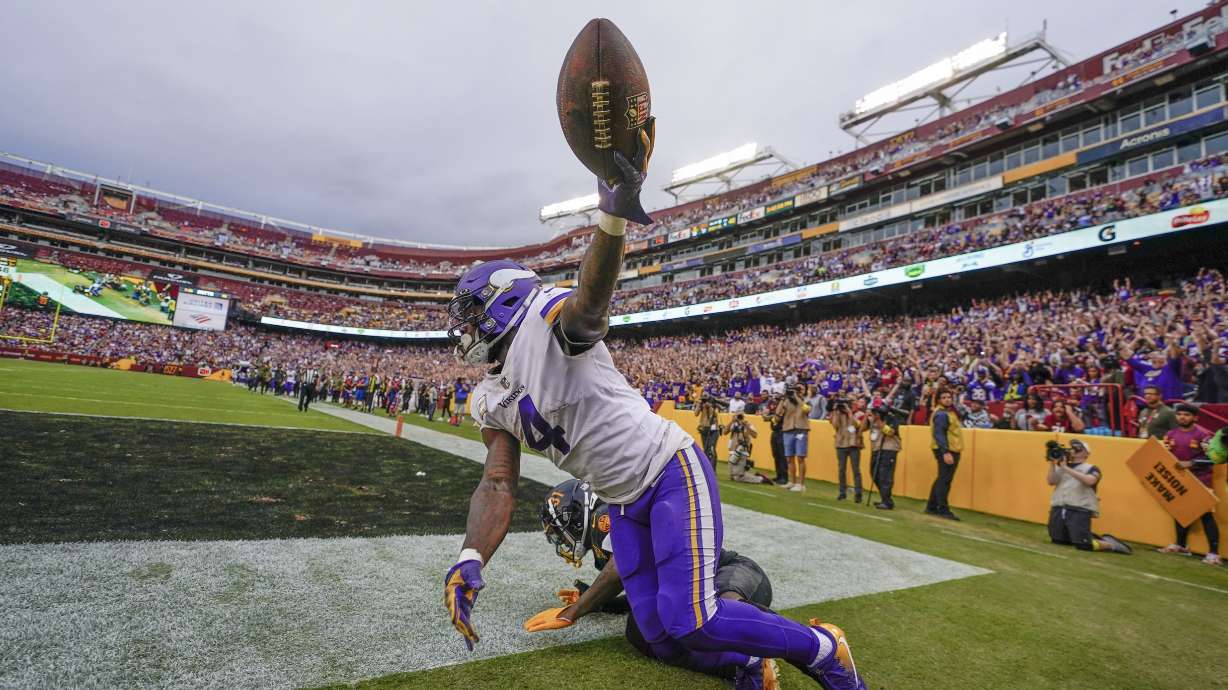 Minnesota Vikings running back Dalvin Cook (4) holds up the ball in the air after making a touchdown catch against Washington Commanders safety Kamren Curl (31) during the second half of an NFL football game, Sunday, Nov. 6, 2022, in Landover, Md.
