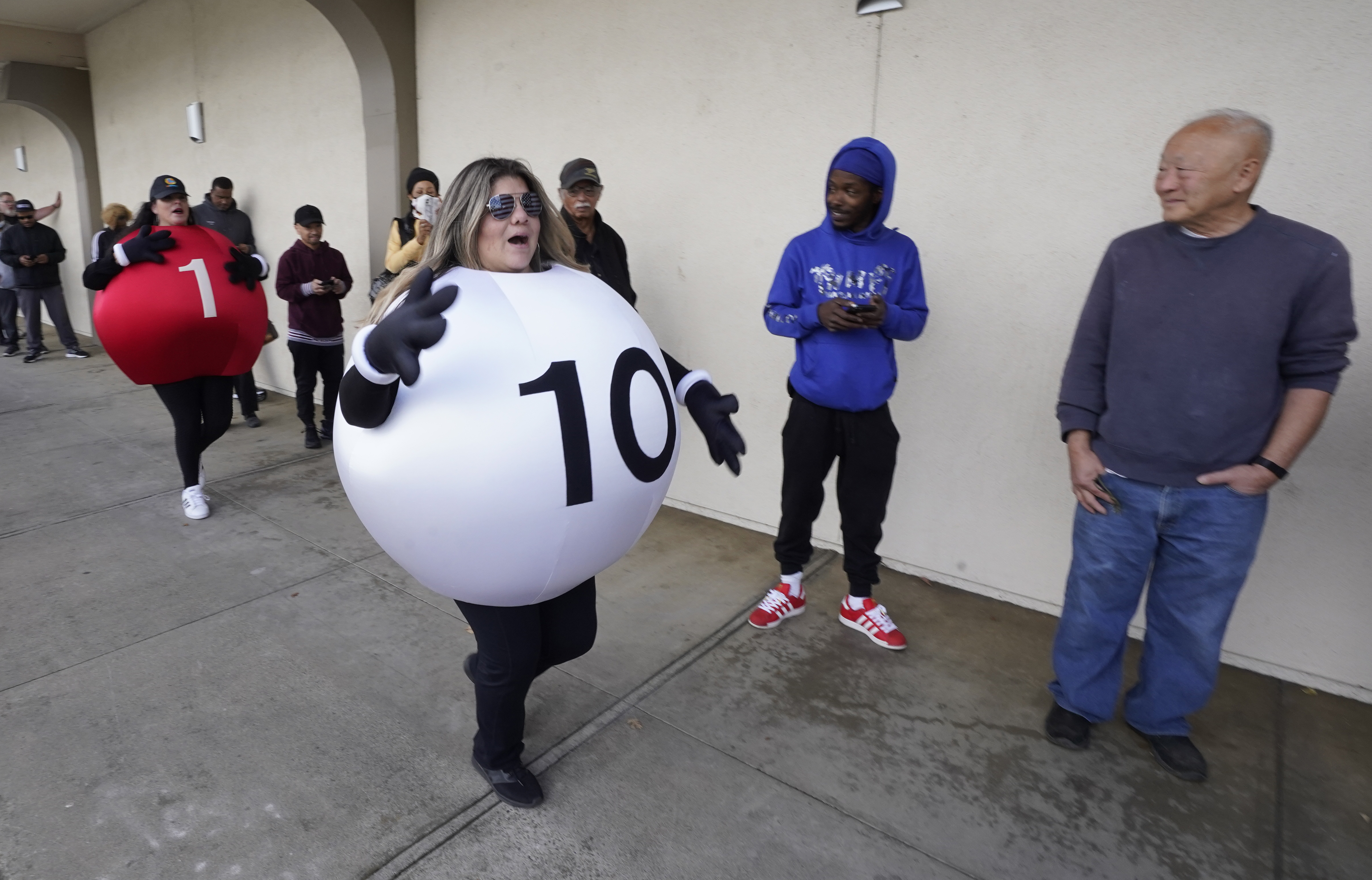 Dressed as Lotto balls, California Lottery employees Marina Maldonado, right, and Liza Solis, left, dance past people waiting to buy Powerball tickets at Lichine's Liquor & Deli in Sacramento, Calif., Monday.