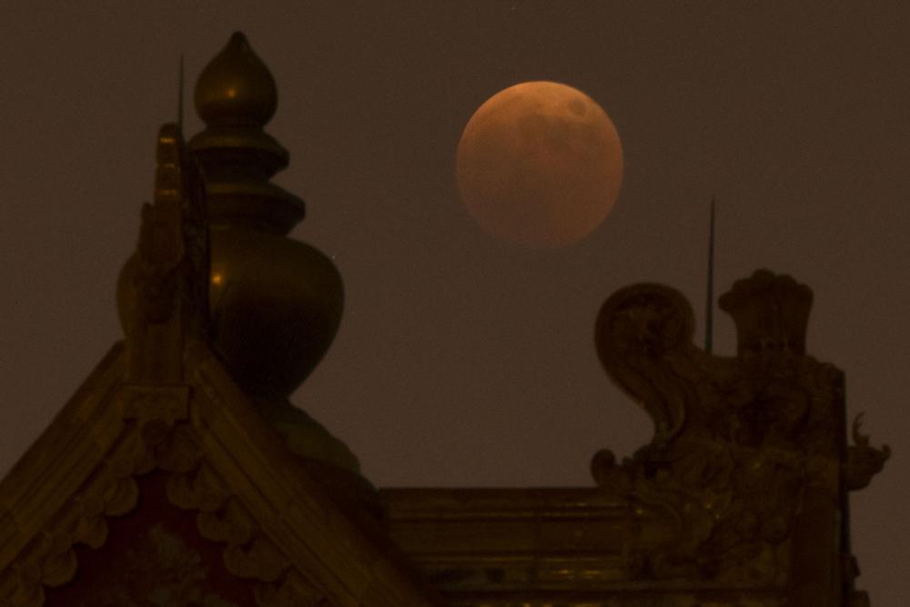 The moon rises behind a corner tower along the outer walls of the Forbidden City during a lunar eclipse in Beijing, Tuesday.