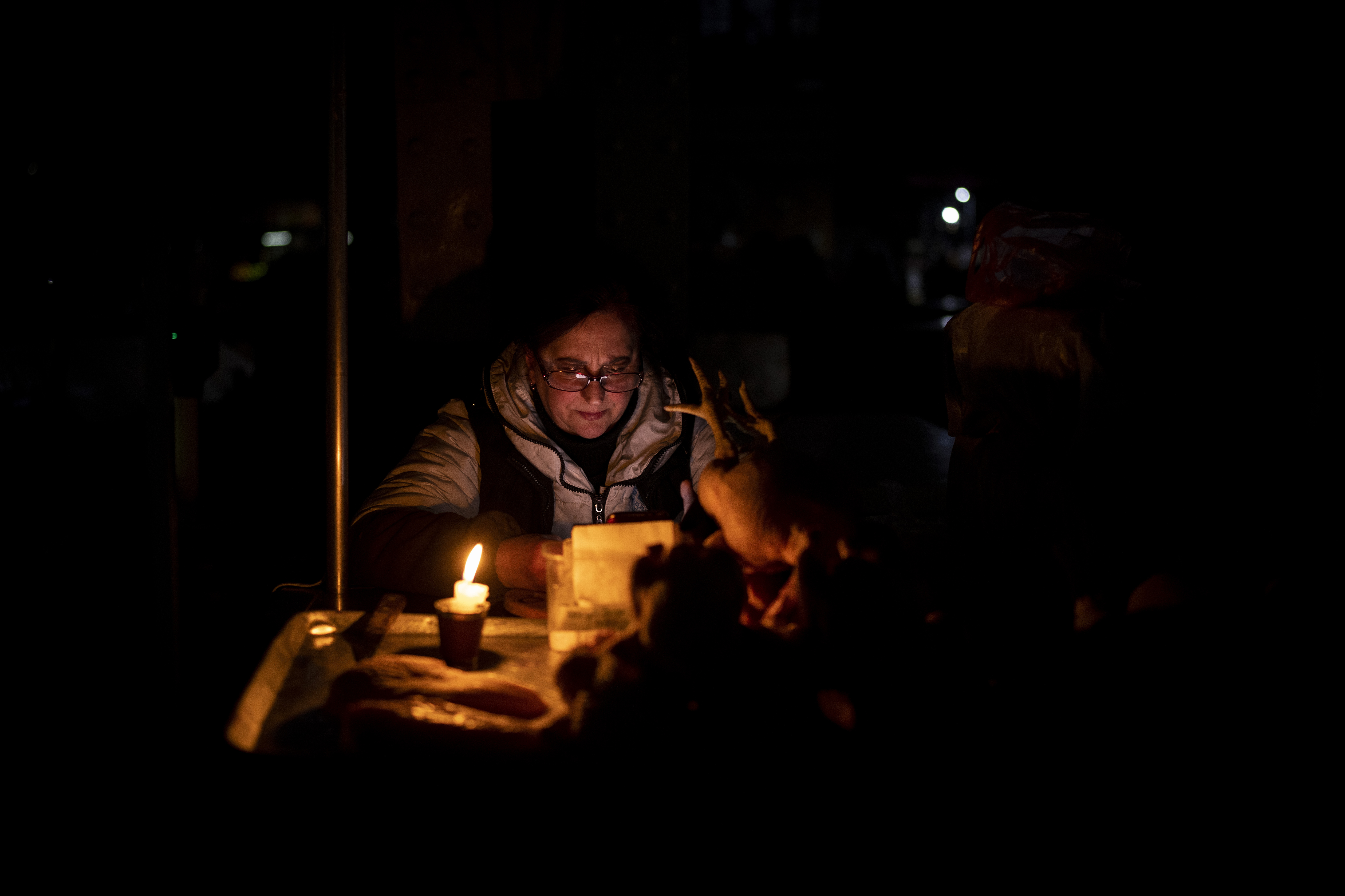 A meat vendor uses a candle to illuminate her market meat stall during a power outage in central Kyiv, Ukraine, Wednesday.