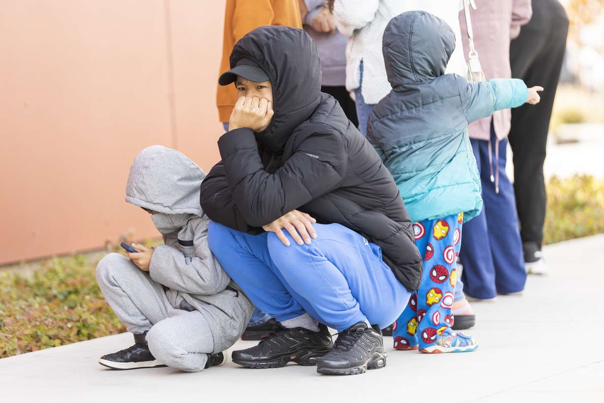 Thaw Reh, center, squats with his son, Moses, 6, left, while they wait outside of the Salt Lake County Library for new winter coats being given out by Operation Warm in South Salt Lake on Saturday.