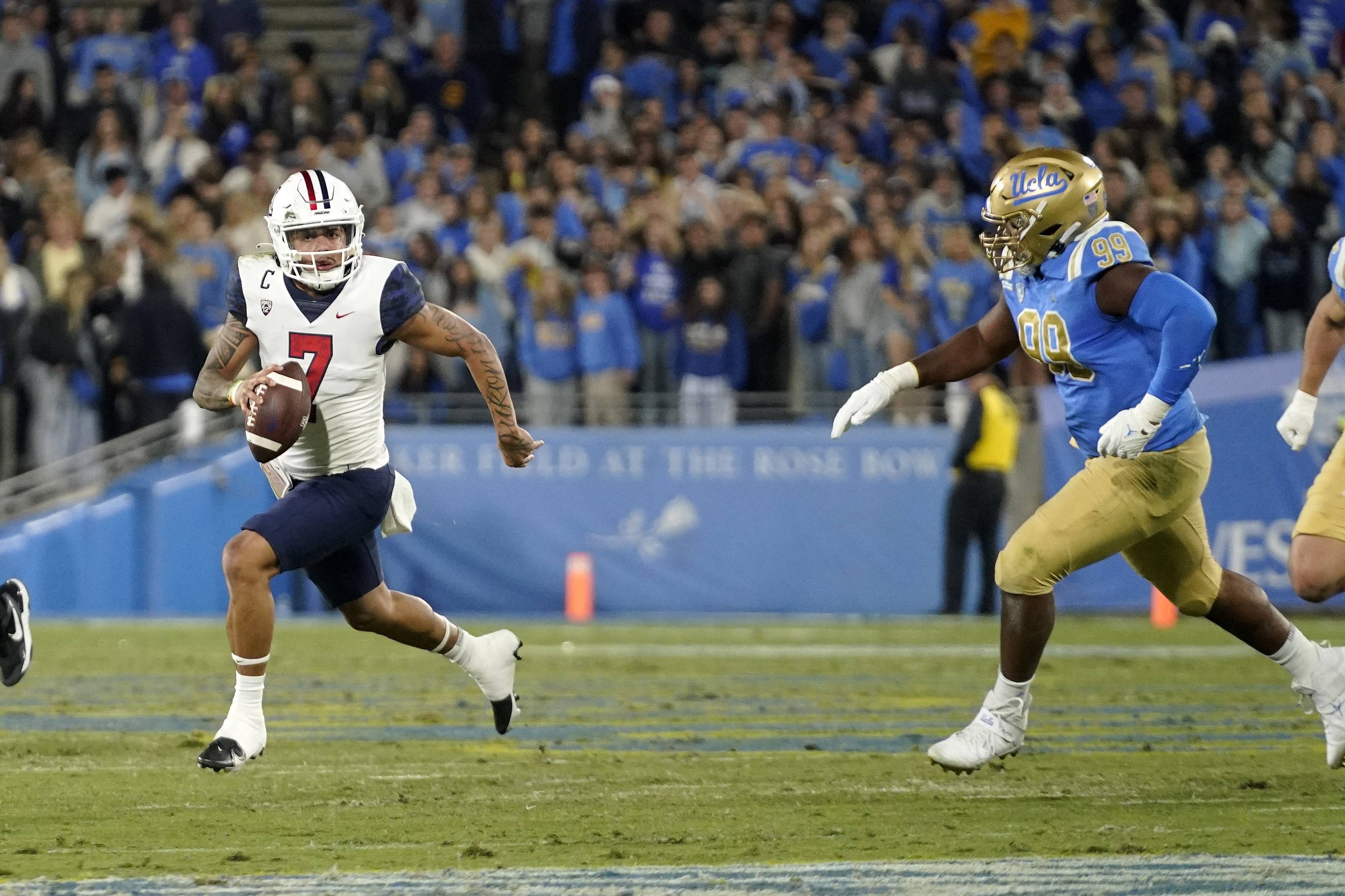 Arizona quarterback Jayden de Laura, left, runs the ball as UCLA defensive lineman Jacob Sykes gives chase during the first half of an NCAA college football game Saturday, Nov. 12, 2022, in Pasadena, Calif.