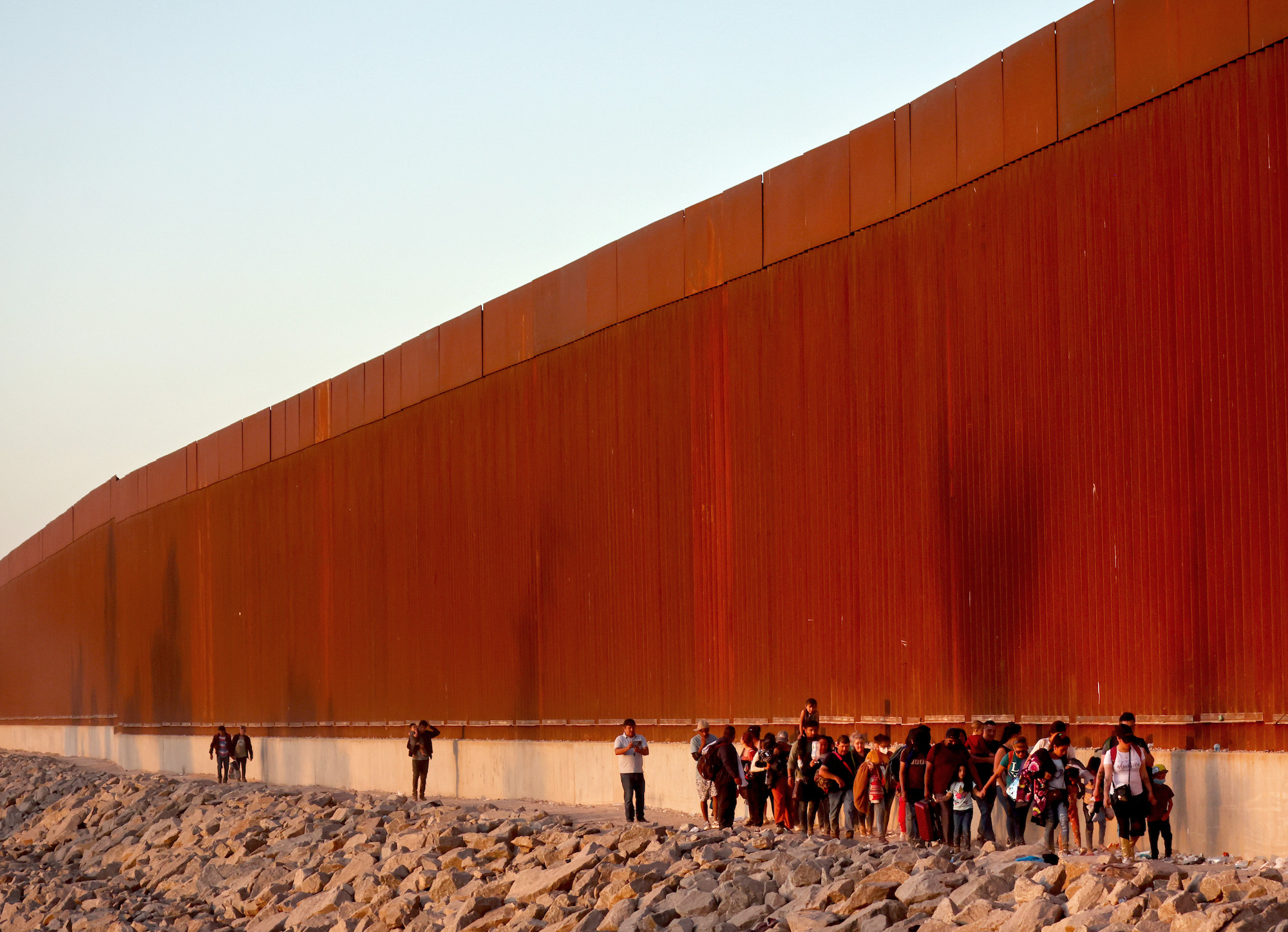 Immigrants walk along the US-Mexico border barrier on their way to await processing by the Border Patrol after crossing from Mexico on May 21, in Yuma, Arizona.