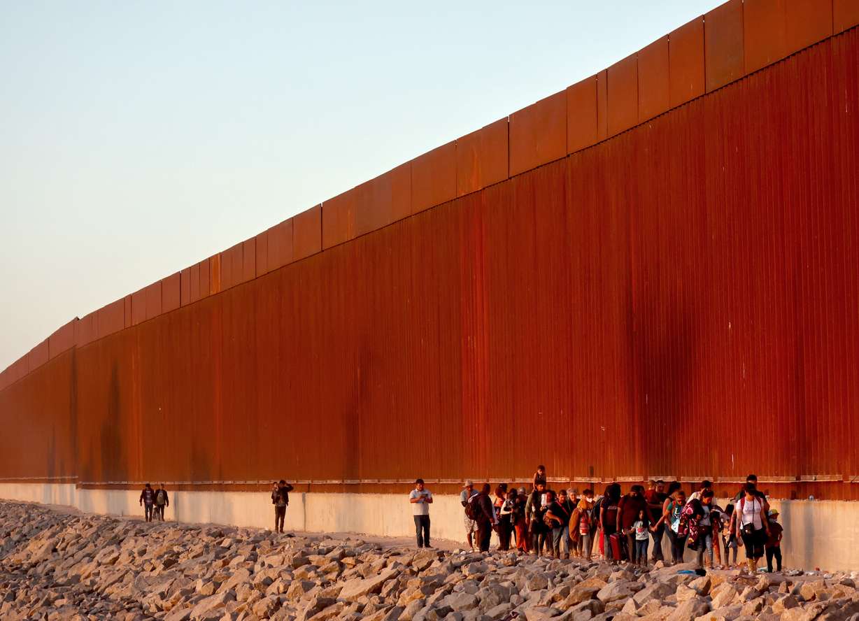 Immigrants walk along the US-Mexico border barrier on their way to await processing by the Border Patrol after crossing from Mexico on May 21, in Yuma, Arizona.