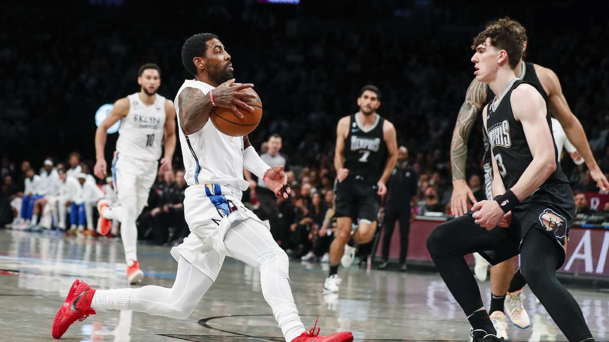 Brooklyn Nets guard Kyrie Irving, left, dribbles against Memphis Grizzlies forward Jake LaRavia (3) during the first half of an NBA basketball game Sunday, Nov. 20, 2022, in New York.