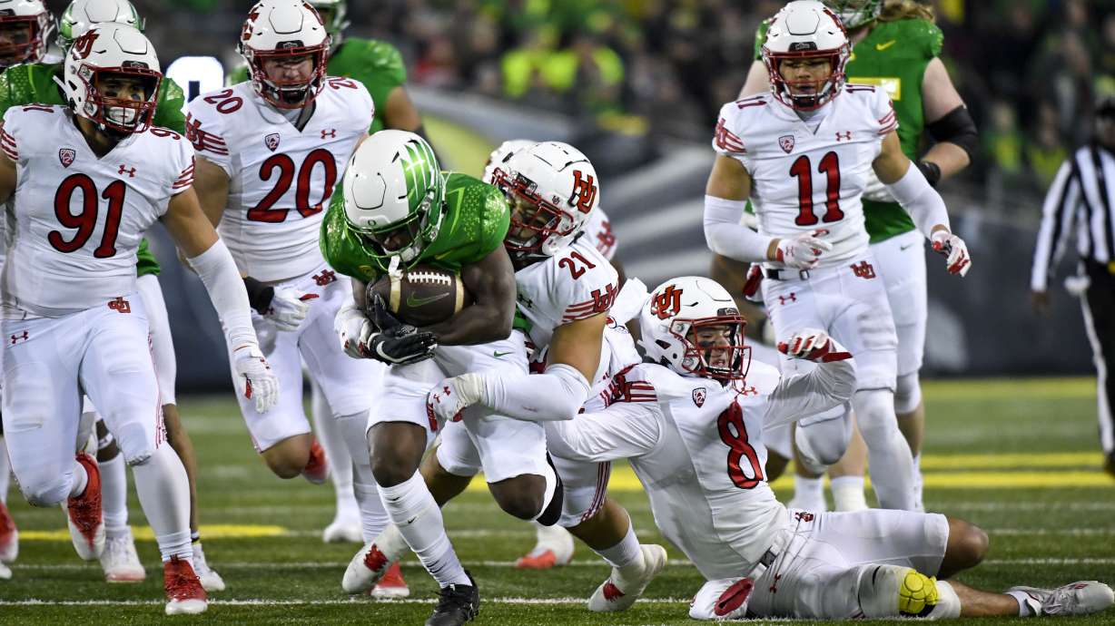 Oregon running back Noah Whittington (22) is tackled by Utah linebacker Karene Reid (21) and safety Cole Bishop (8) as defensive end Gabe Reid (91), linebacker Lander Barton (20) and safety R.J. Hubert (11) trail on the play during the first half of an NCAA college football game Saturday, Nov. 19, 2022, in Eugene, Ore.