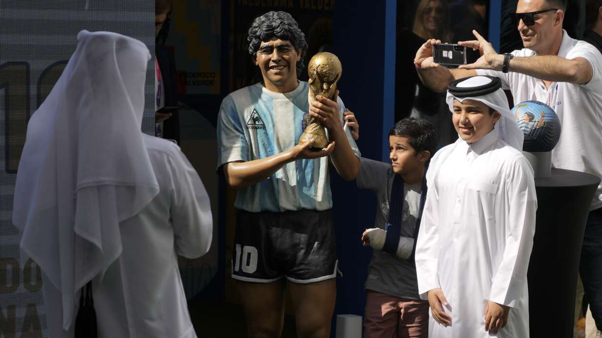 Children pose for a picture with a statue of the late soccer star Diego Maradona during a commemoration in his honor in Doha, in Friday, Nov. 25, 2022.
