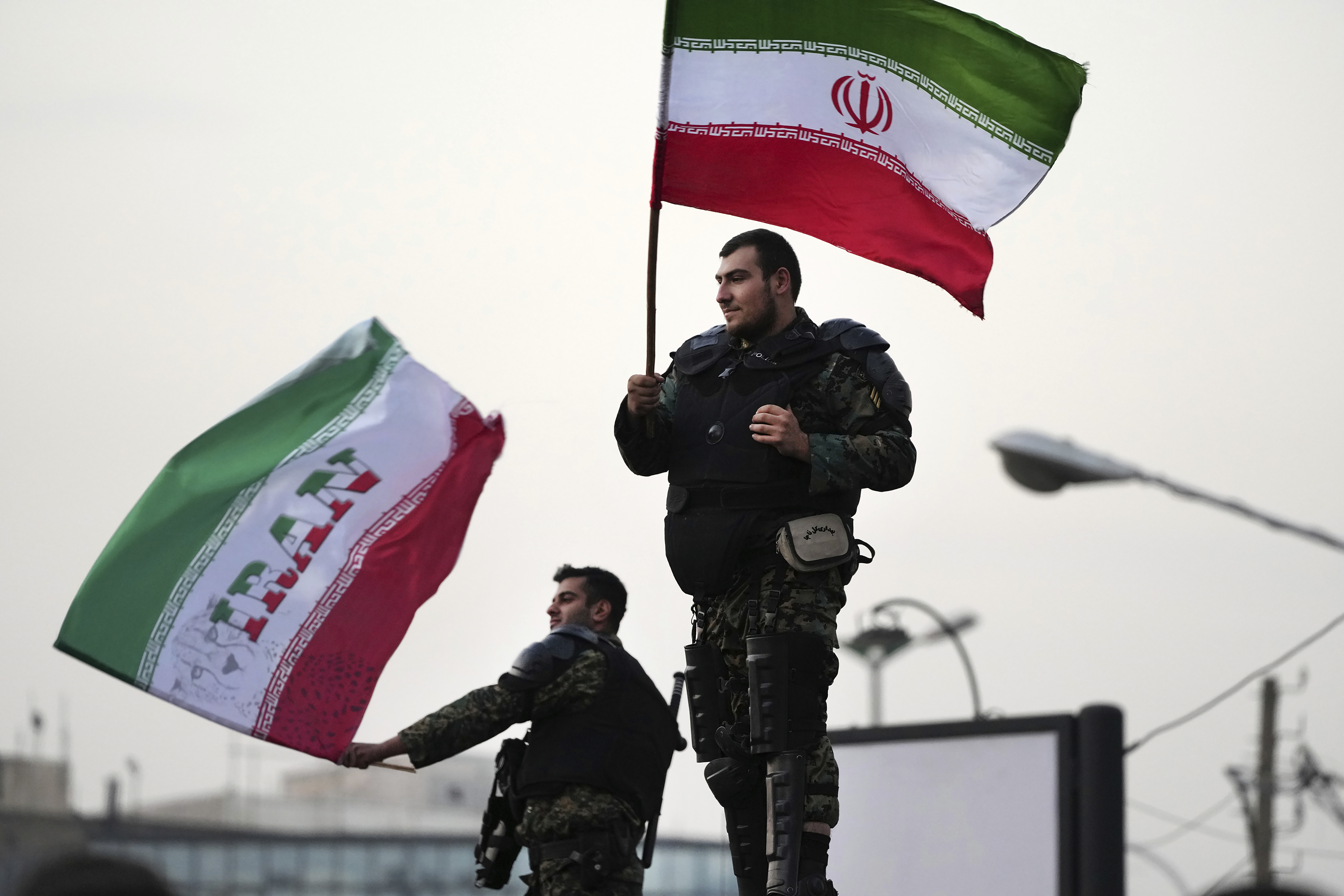 Two anti-riot police officers wave the Iranian flags during a street celebration after Iran defeated Wales in Qatar's World Cup, at Sadeghieh Sq. in Tehran, Iran, Friday, Nov. 25, 2022. Iran's political turmoil has cast a shadow over Iran's matches at the World Cup, spurring tension between those who back the team and those who accuse players of not doing enough to support the protests that started Sept. 16 over the death of a 22-year-old woman in the custody of the morality police.