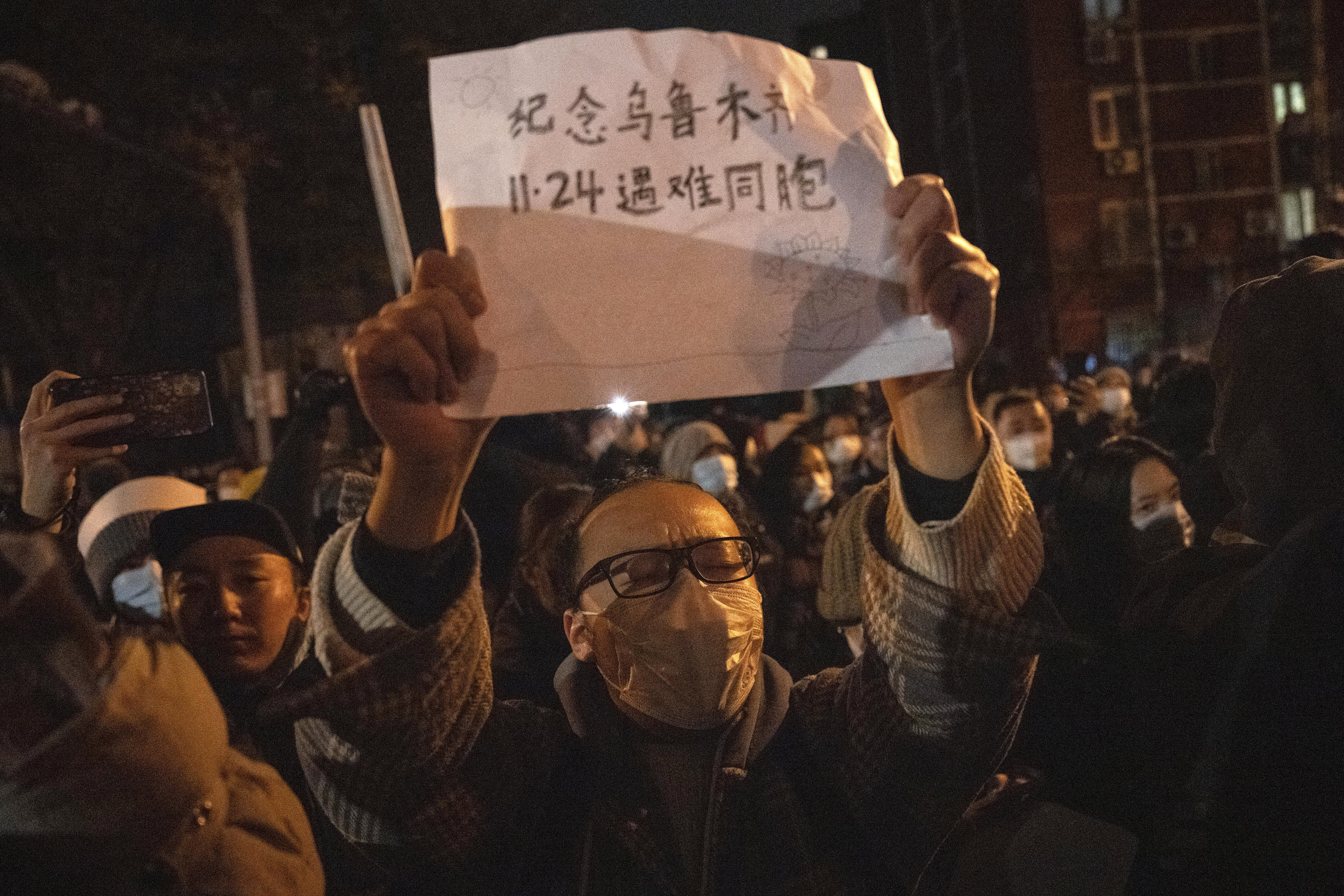 A protester holds up a sign which reads "Commemorate Urumqi Nov 24 compatriots who died" in Beijing, Sunday. Protesters angered by strict anti-virus measures called for China's powerful leader to resign.