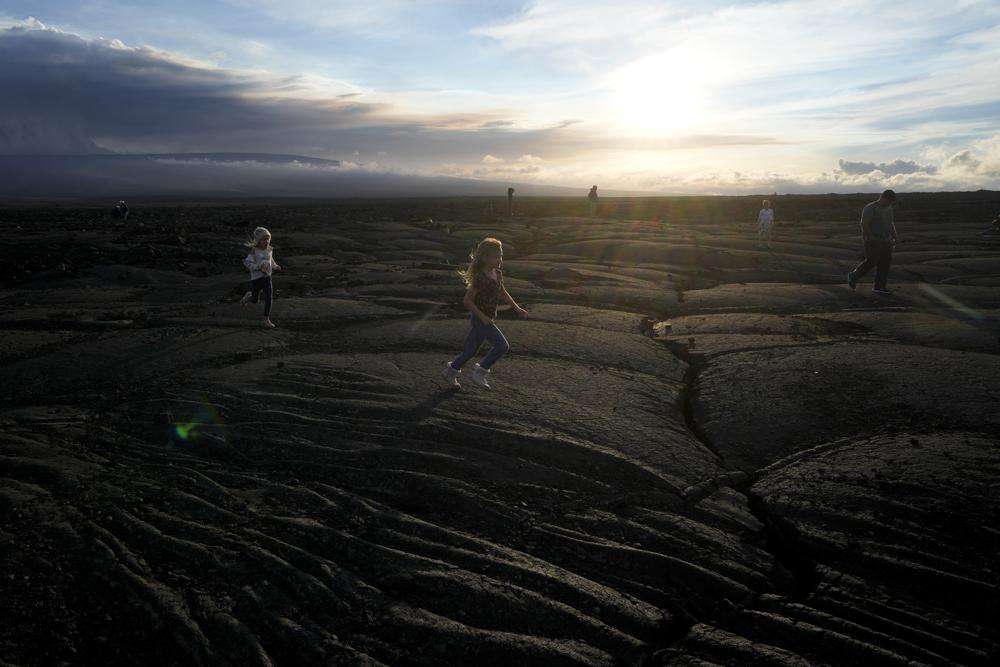 Children run on blackened lava rock from a previous eruption near the Mauna Loa volcano as it erupts Wednesday near Hilo, Hawaii.