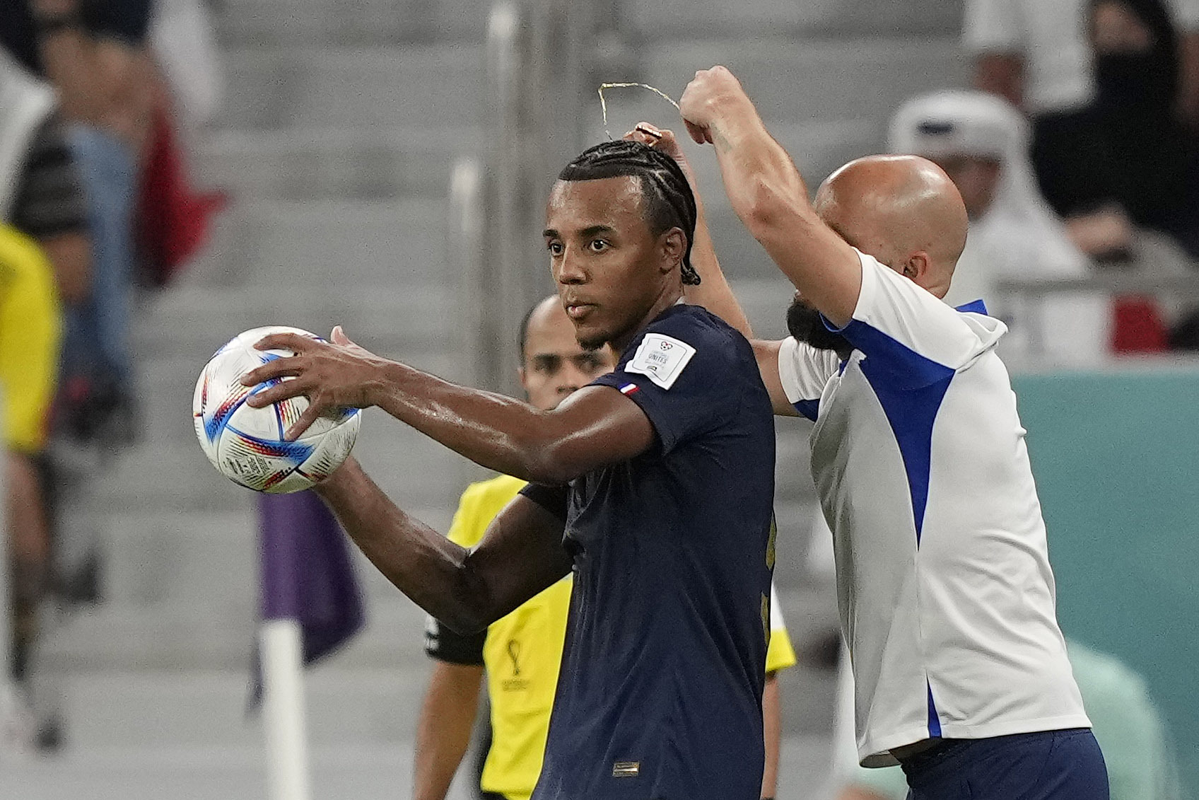 An assistant coach takes of the necklace of France's Jules Kounde during the World Cup round of 16 soccer match between France and Poland, at the Al Thumama Stadium in Doha, Qatar, Sunday, Dec. 4, 2022. 
