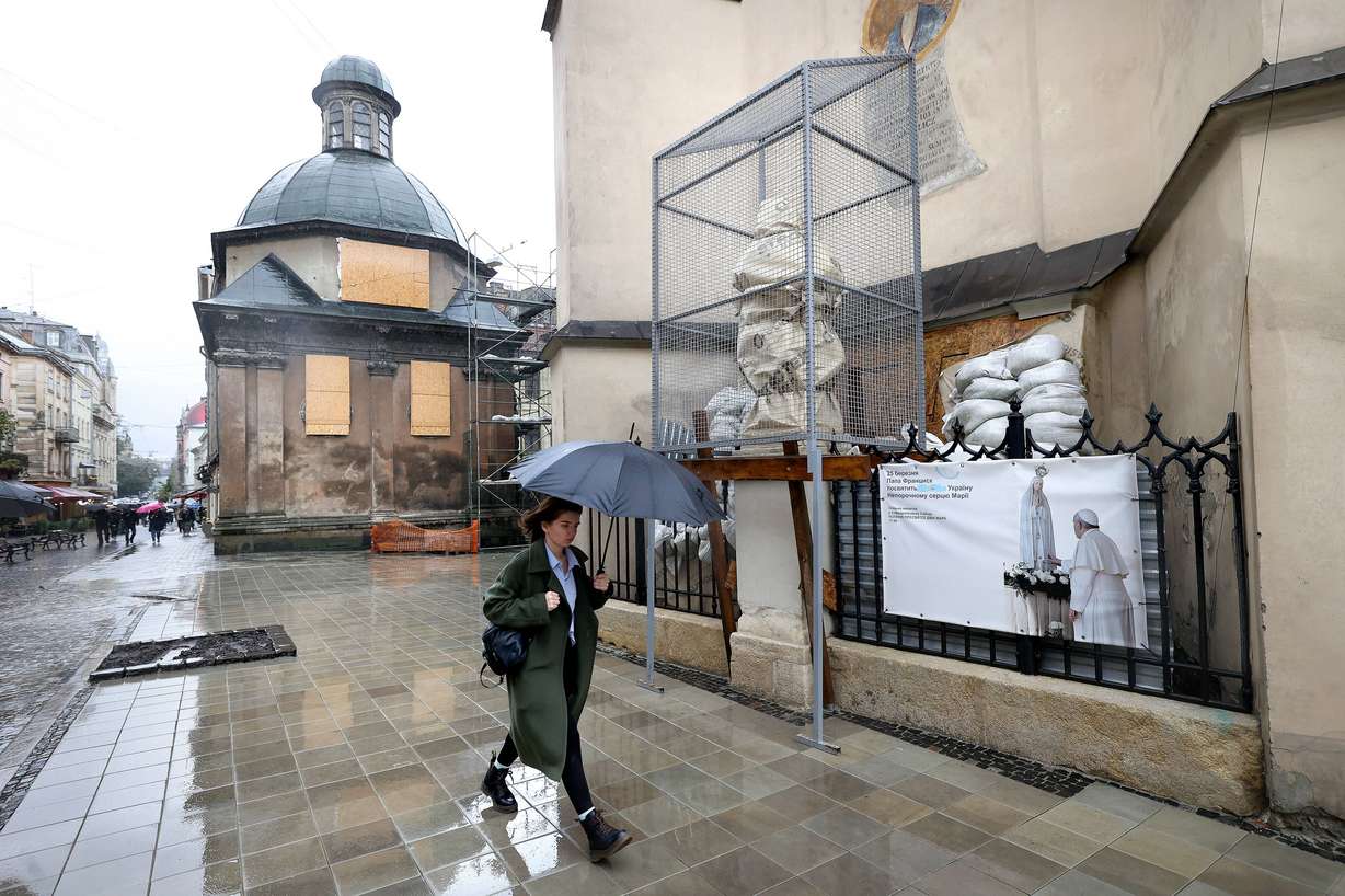 A woman walks past barricaded windows and a statue that has been wrapped in a protective cage outside of the Archcathedral Basilica of the Assumption of the Blessed Virgin Mary in Lviv, Ukraine, on Sept. 18.