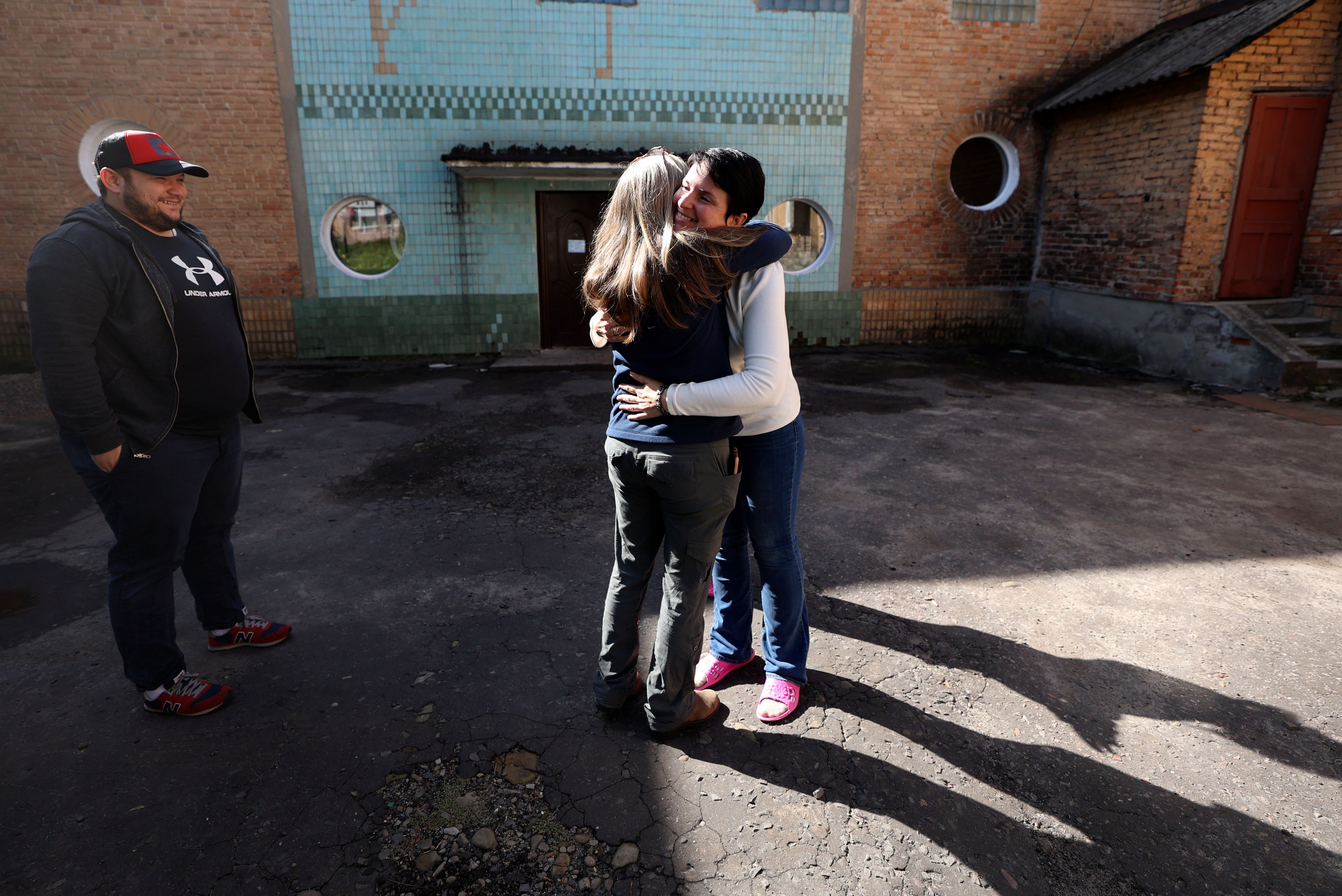 Yurii Slepak, WelcomeNST country director for Ukraine, watches as Liz Davis-Edwards, WelcomeNST CEO, hugs Elvira Karnaukh outside of Chervonohrad Kindergarten No. 12, in Chervonohrad, Ukraine, on Sept. 17. On Sept. 20, Karnaukh left Ukraine with her two children, starting their journey with WelcomeNST to Lehi, Utah.